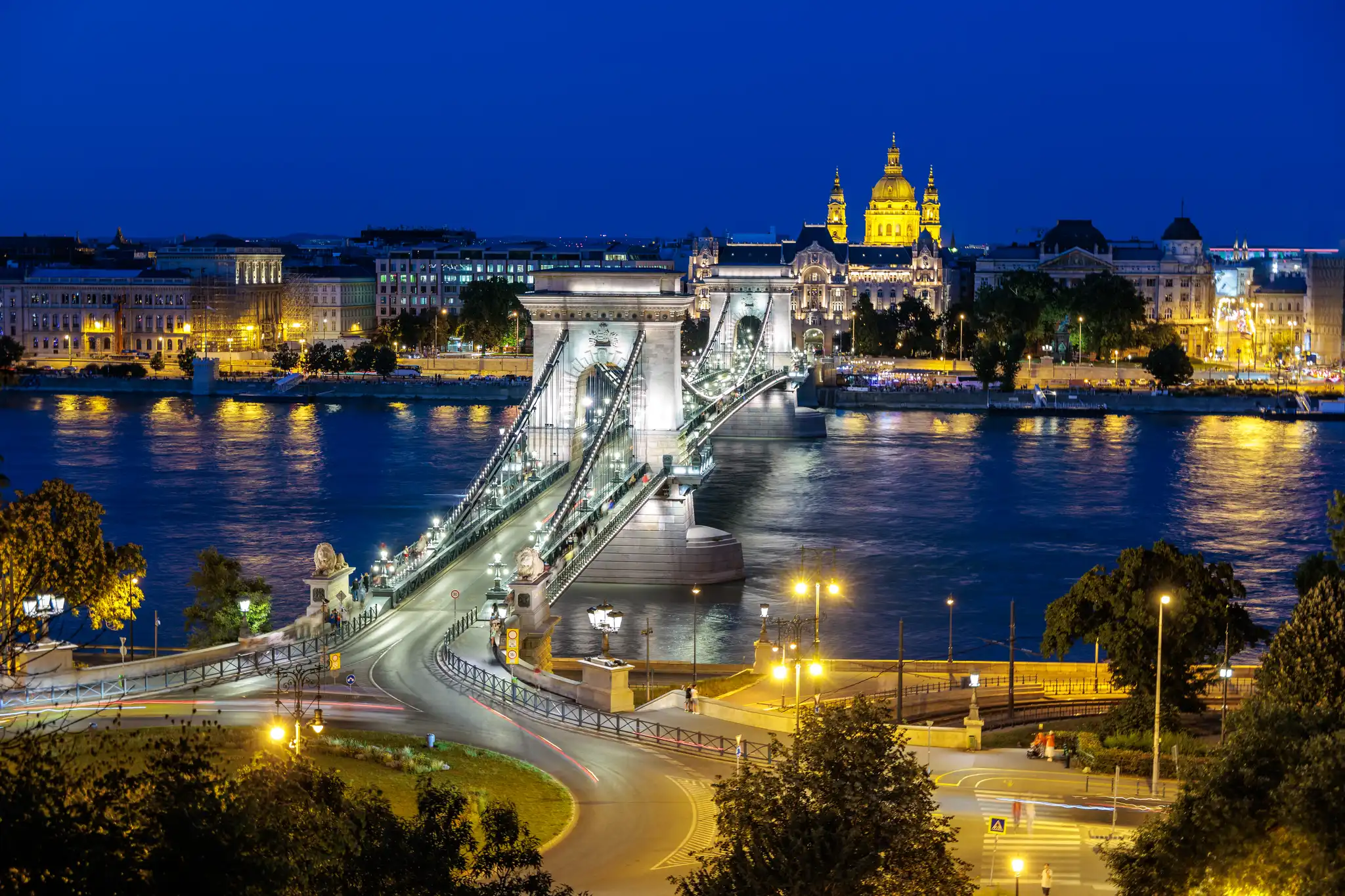 Beleuchtete Kettenbrücke und St.-Stephans-Basilika in Budapest bei Nacht über der Donau mit Lichtspuren.