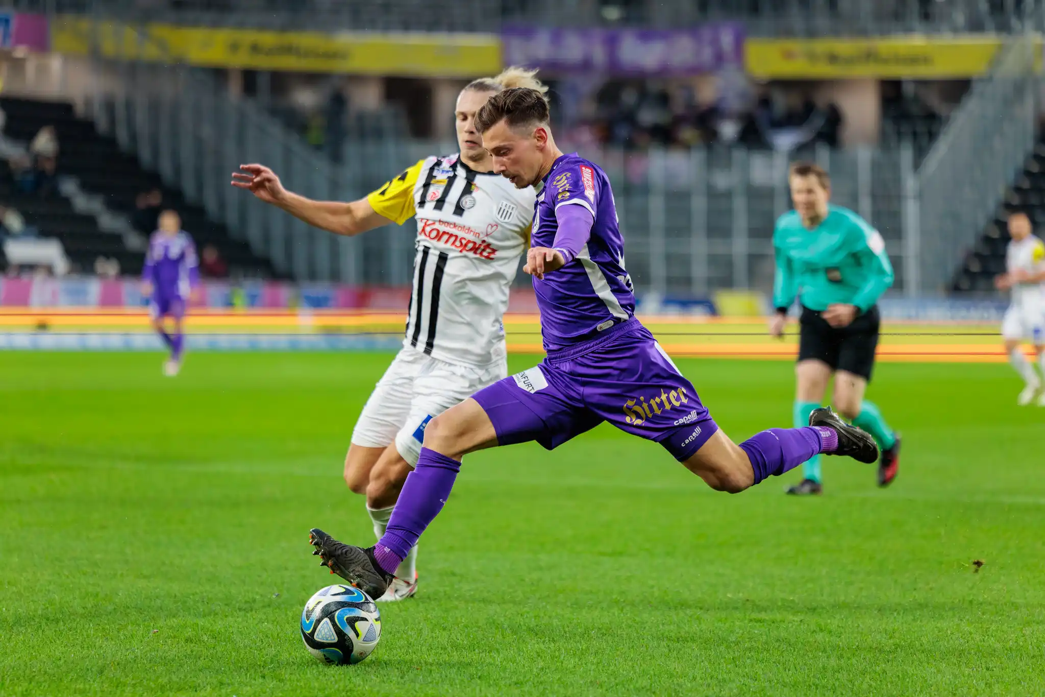 Ein Fußballspieler im lila Trikot tritt den Ball während eines Bundesligaspiels in der Raiffeisen Arena 