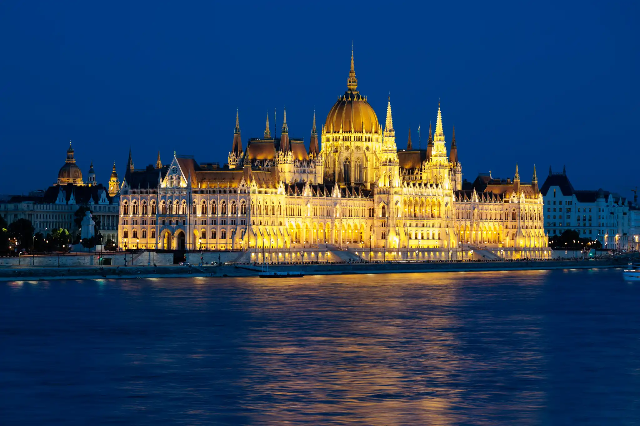 Nachtansicht des beleuchteten Ungarischen Parlamentsgebäudes in Budapest an der Donau, mit goldener Kuppel und hellen Lichtern, die sich im Wasser spiegeln.