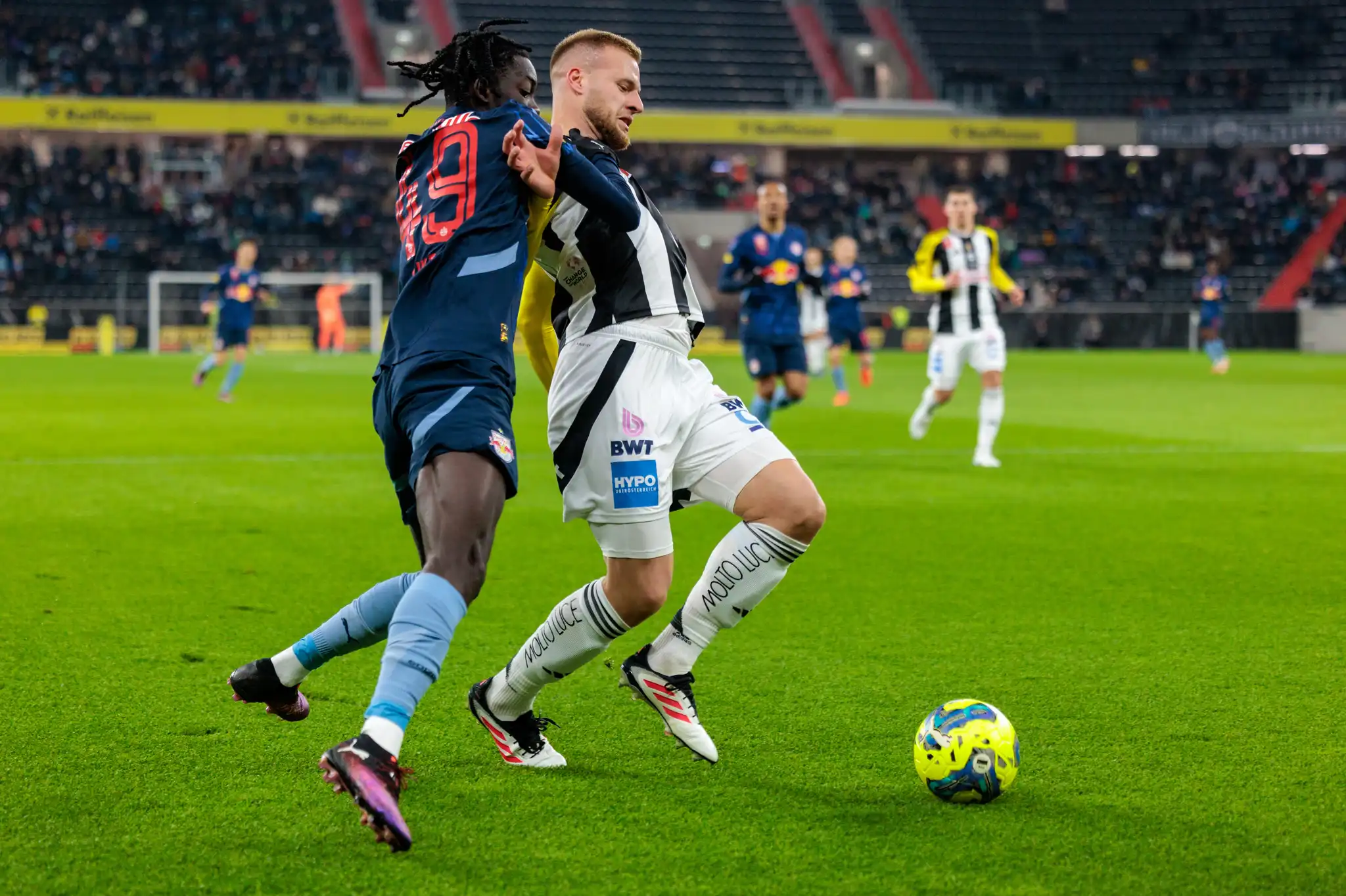 Zwei Fußballspieler im intensiven Zweikampf um den Ball: Ein Red Bull Salzburg Spieler und LASK Spieler in der Raiffeisen Arena
