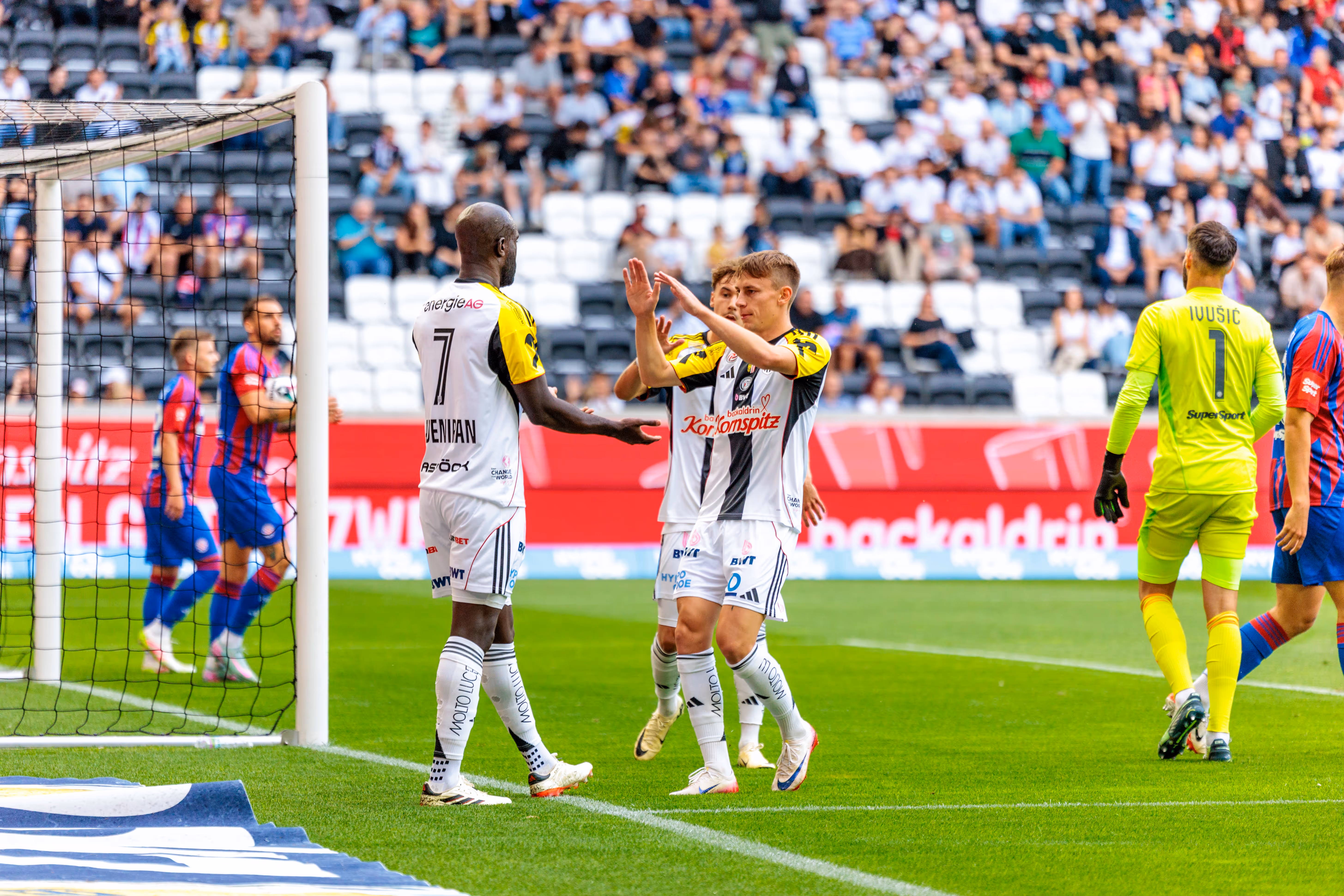 LASK Fußballspieler im schwarz-weißen Trikot feiern einen Torerfolg während eines Spiels der Nero Summer Series in der Raiffeisen Arena vor einer Tribüne voller Zuschauer