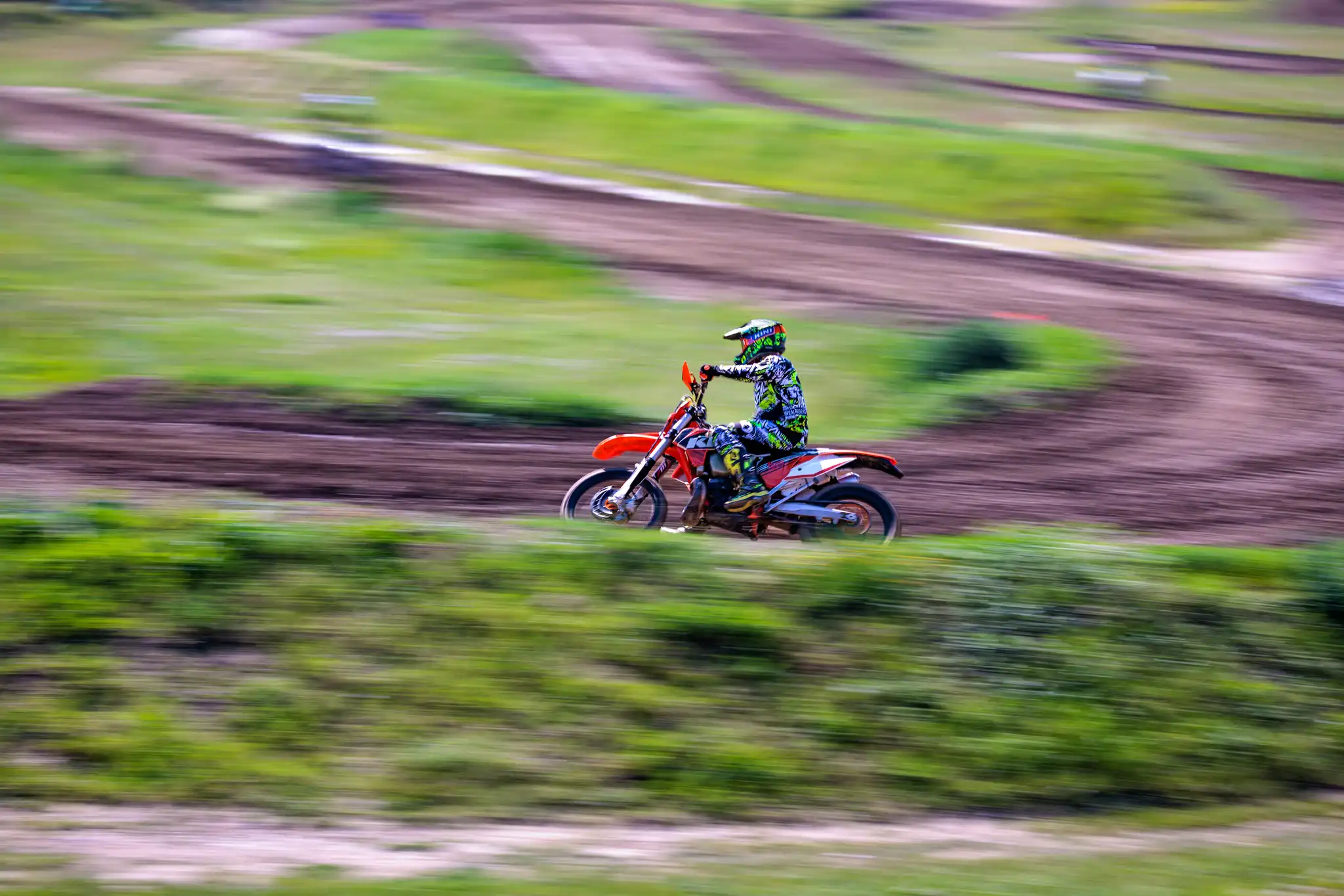 Mitzieher eines Motocrossfahrer in voller Fahrt auf orangefarbenem Dirt Bike auf einer Motocrossstrecke