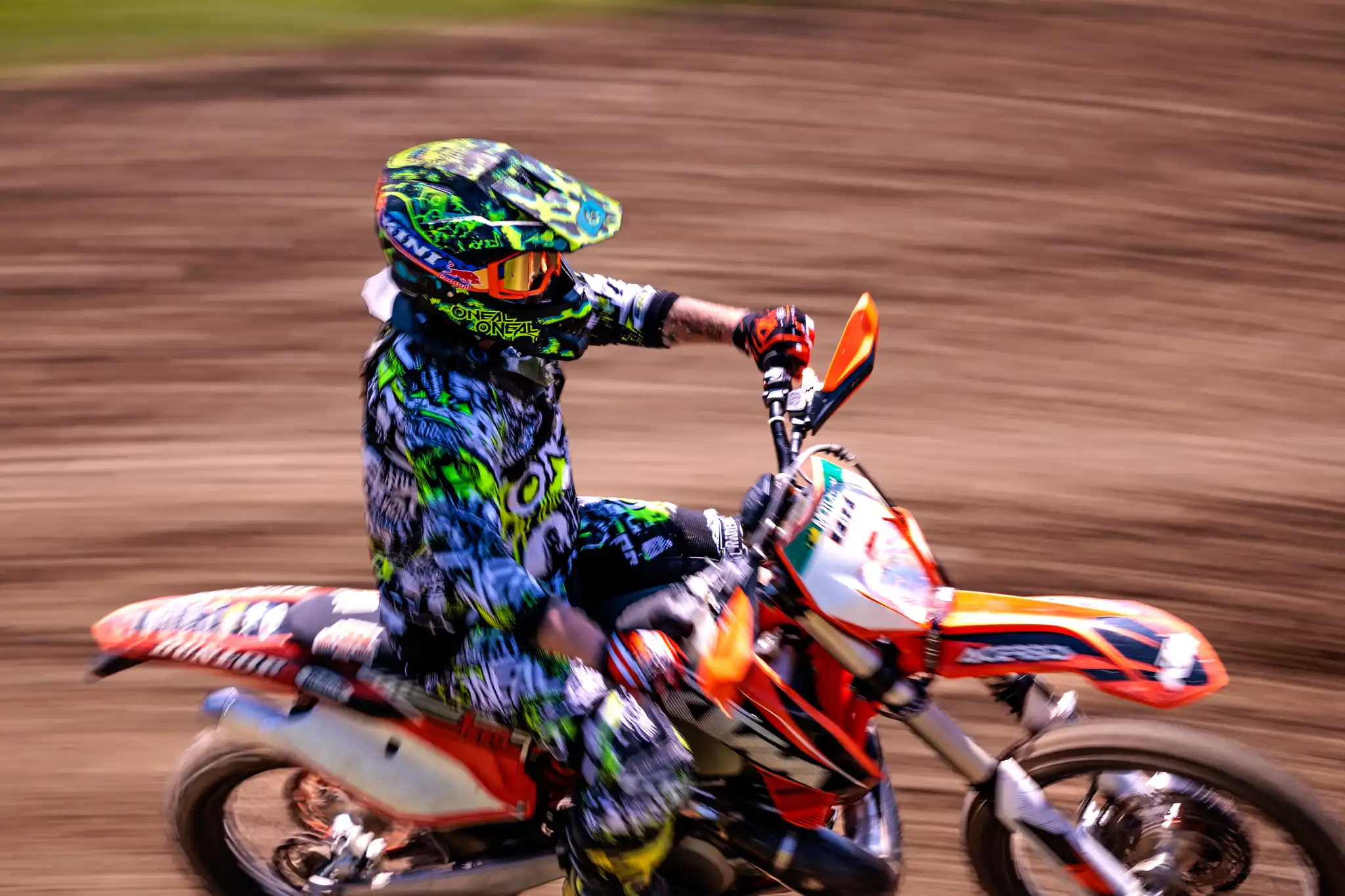 Motocross-Fahrer mit neonfarbenem Helm und Schutzkleidung auf einem orangen Dirtbike in schneller Fahrt