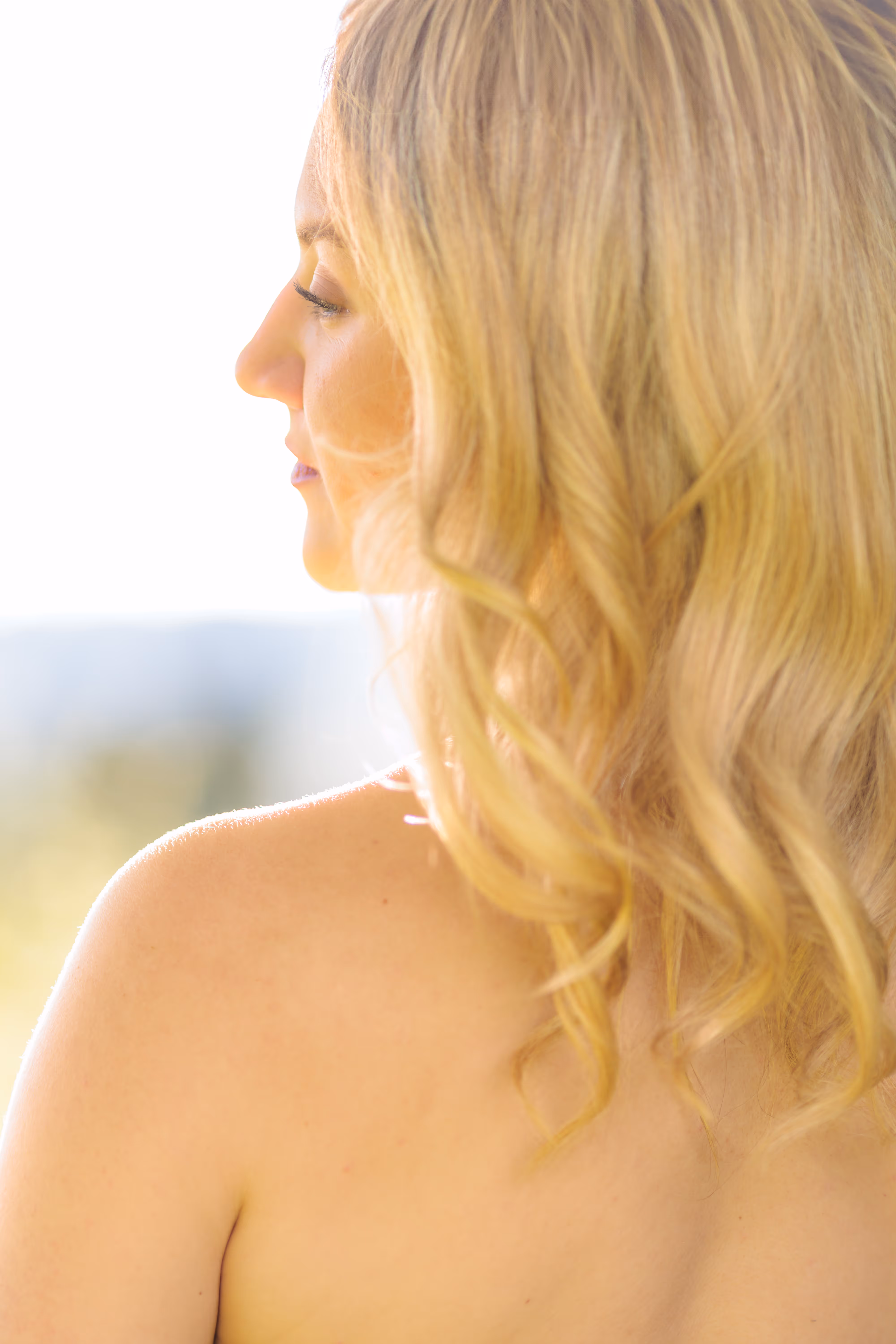 Eine blonde Frau ist im Profil zu sehen, ihr gewelltes Haar und ihre Schulter werden von warmem Gegenlicht sanft beleuchtet