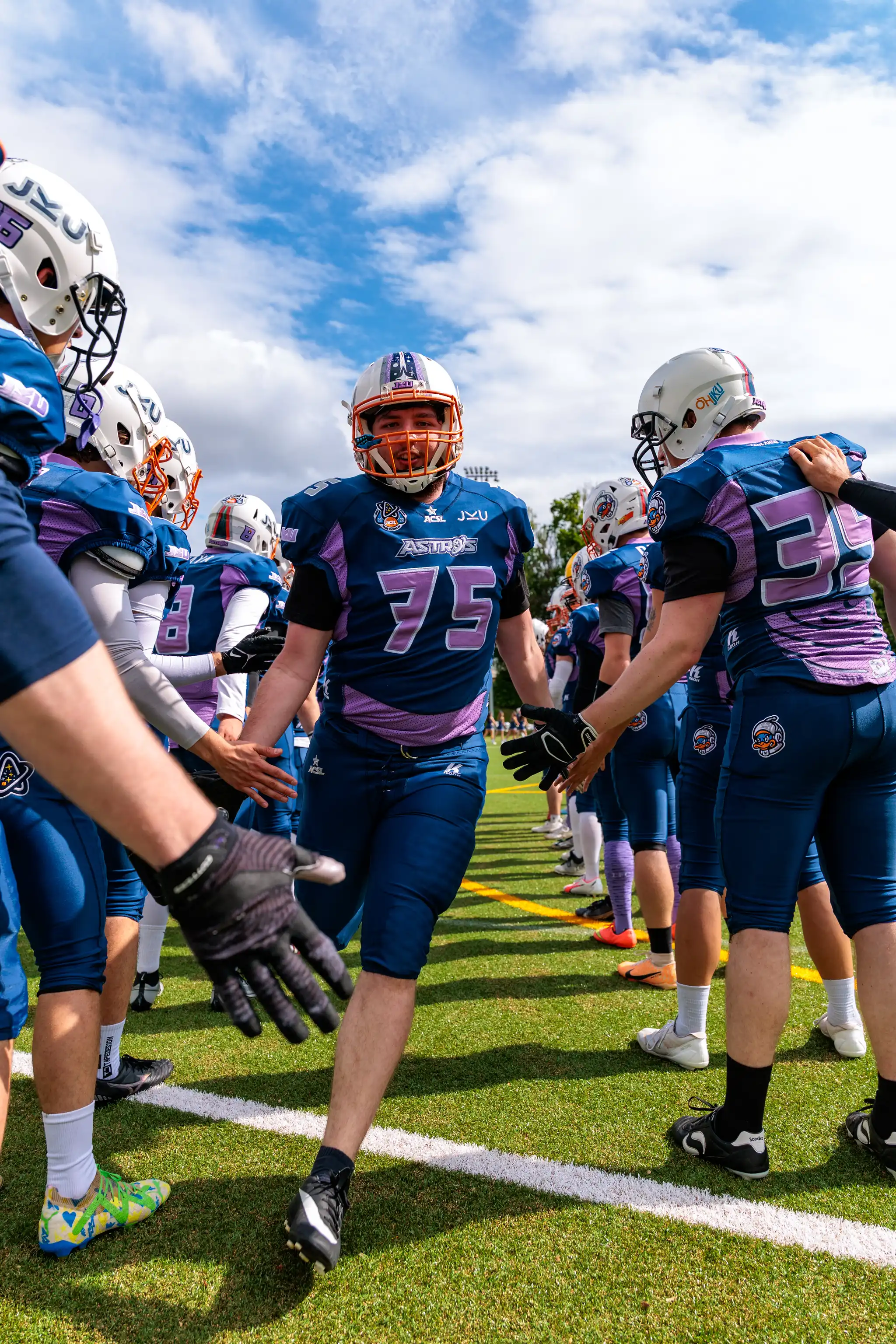 Ein American-Football-Spieler in blau-lila Uniform mit der Nummer 75 läuft durch eine Reihe von Spielern, die sich per Handschlag begrüßen