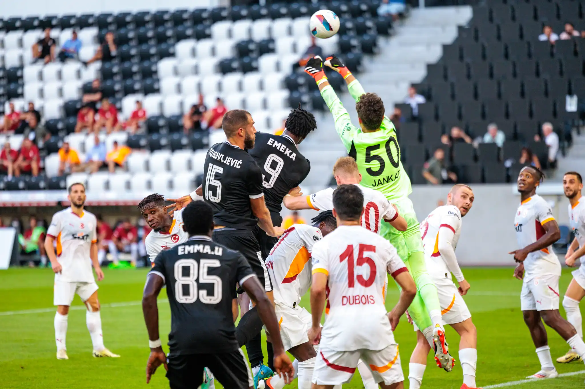 Ein Torhüter im leuchtend grünen Trikot springt nach einem Fußball, umgeben von Spielern in schwarzen und weißen Trikots, die in der Raiffeisen Arena um den Ballbesitz kämpfen