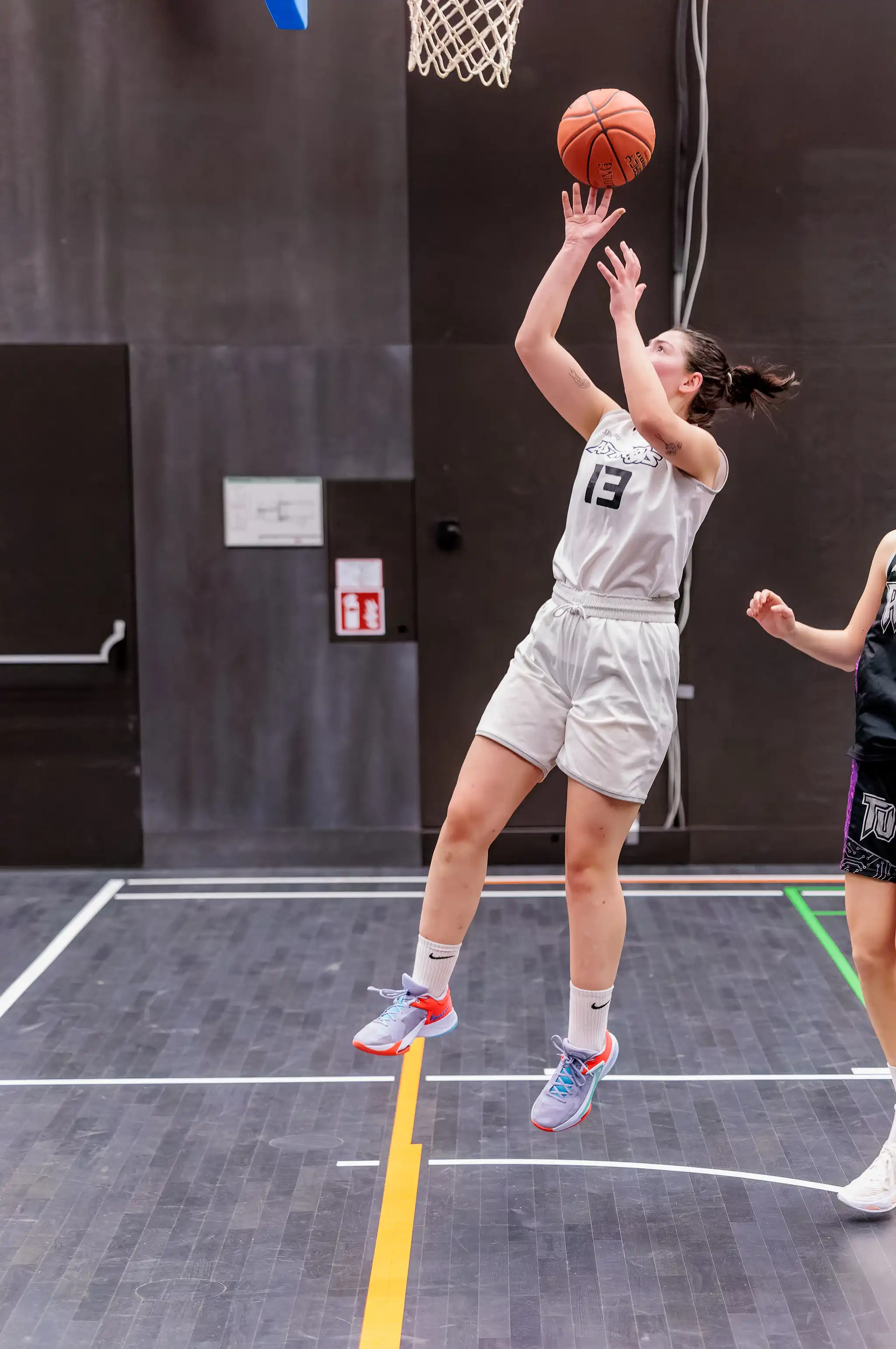 Eine Basketballspielerin im Trikot mit der Nummer 13 springt während eines Spiels zum Korbwurf