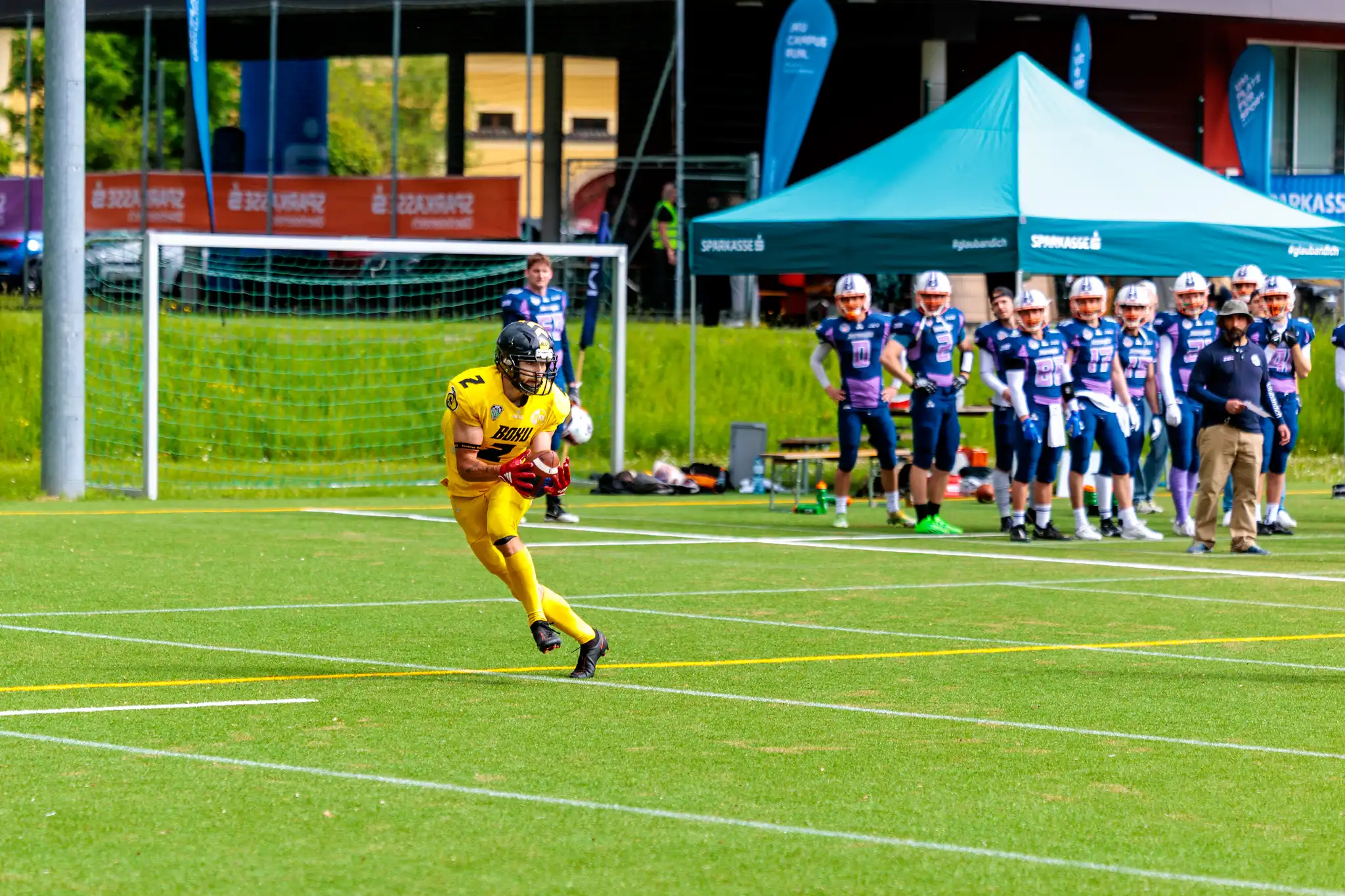 Ein American-Football-Spieler in gelbem Trikot läuft mit dem Ball über das grüne Feld