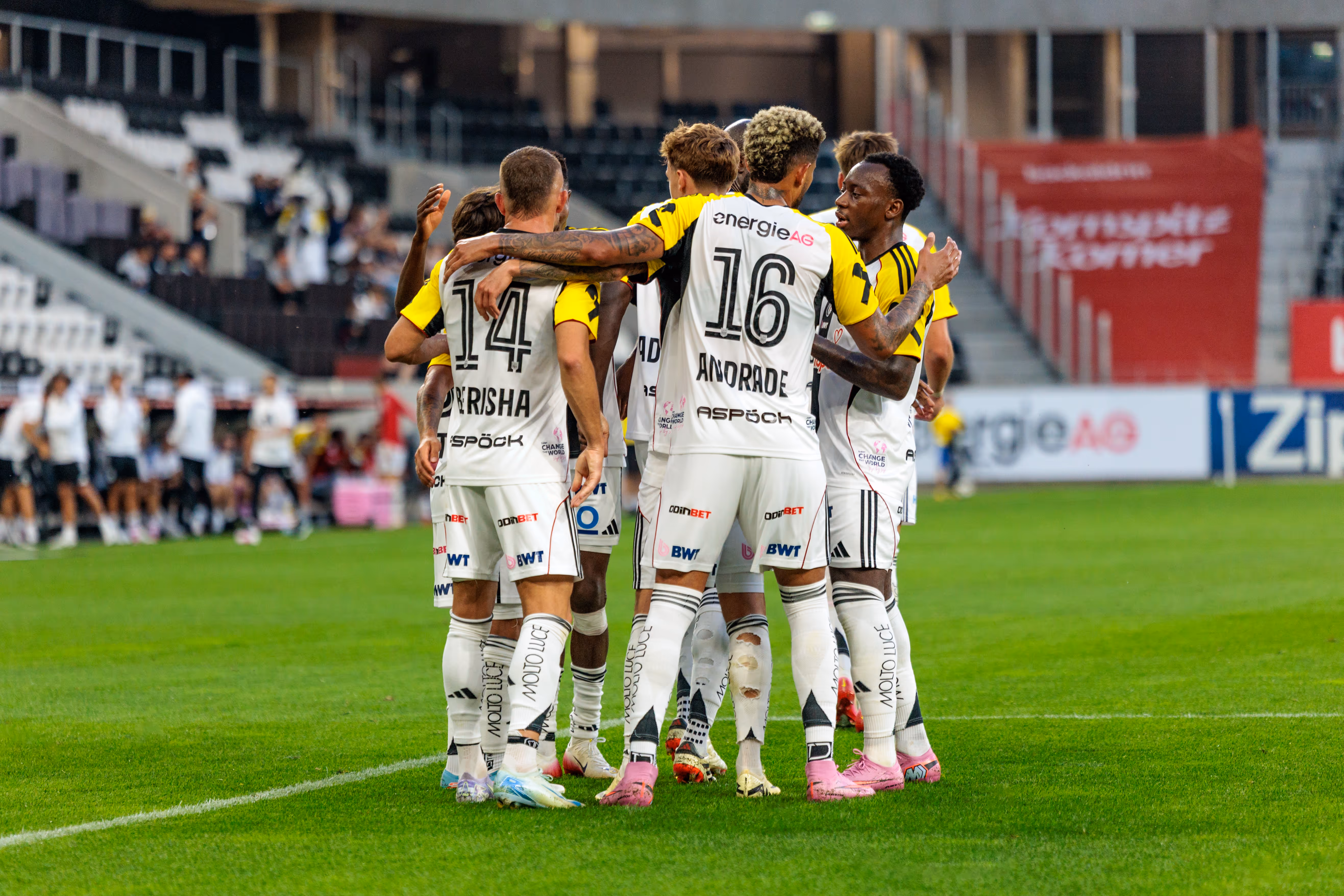 Mehrere LASK Fußballspieler in hellen Trikots bilden während eines Nero Summer Series Vorbereitungsspiels einen engen Kreis auf dem Spielfeld