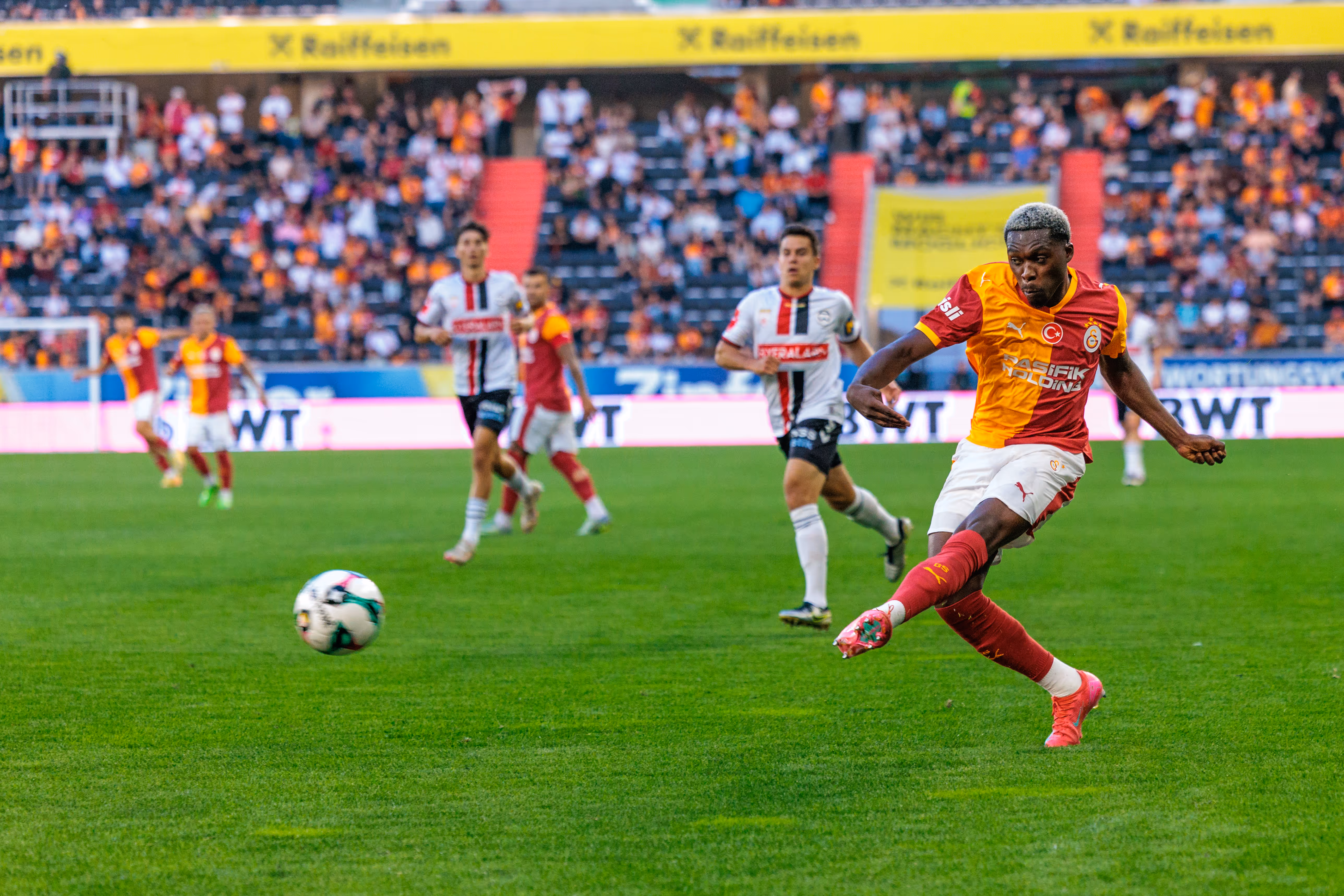 Ein Fußballspieler von Galatasaray Istanbul tritt den Ball während eines Spiels in der Raiffeisen Arena vor einer gefüllten Tribüne
