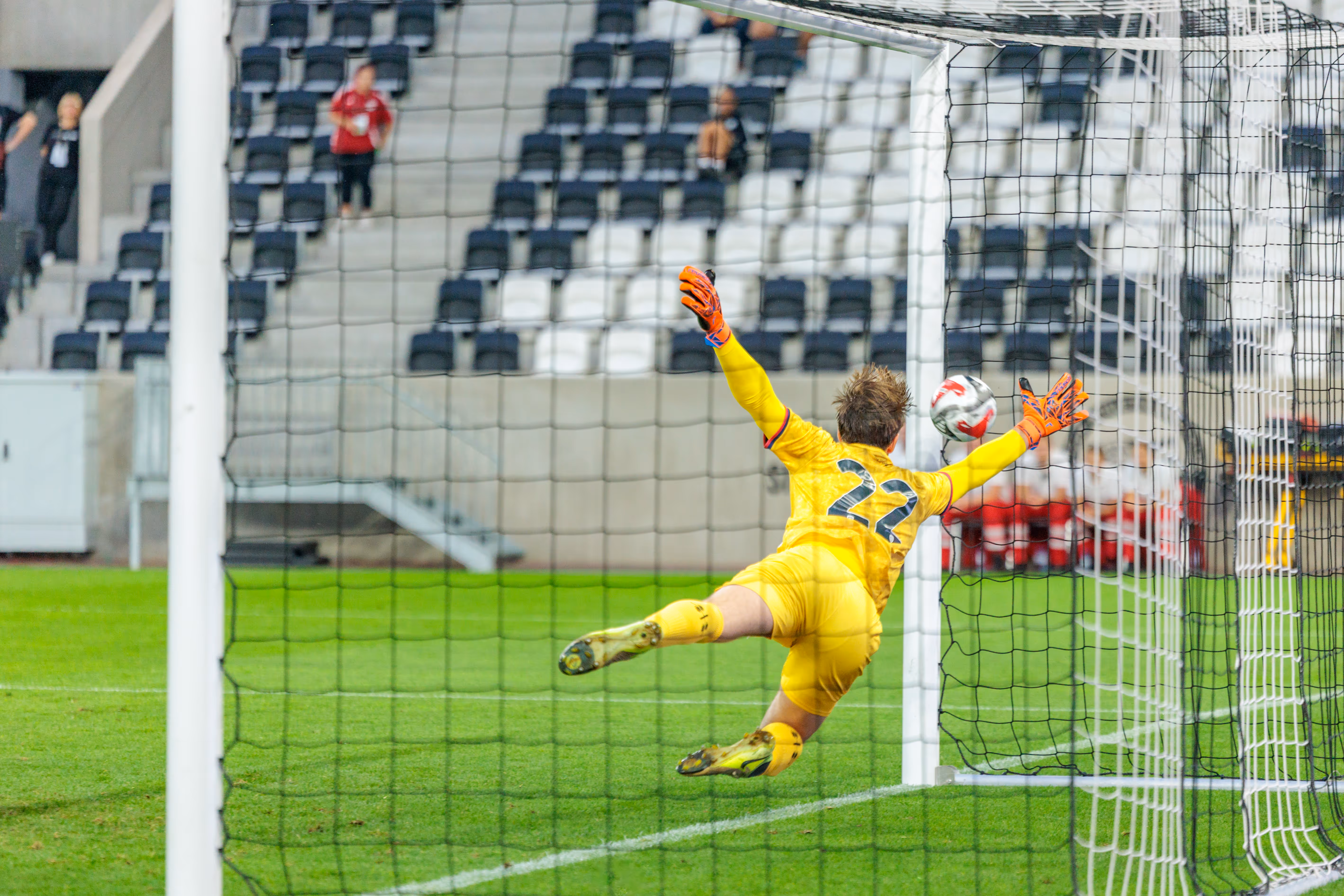 Ein Fußballtorhüter in gelbem Trikot mit der Nummer 22 pariert mit orangefarbenen Handschuhen einen Ball während eines spannenden Spiels der Nero Summer Series