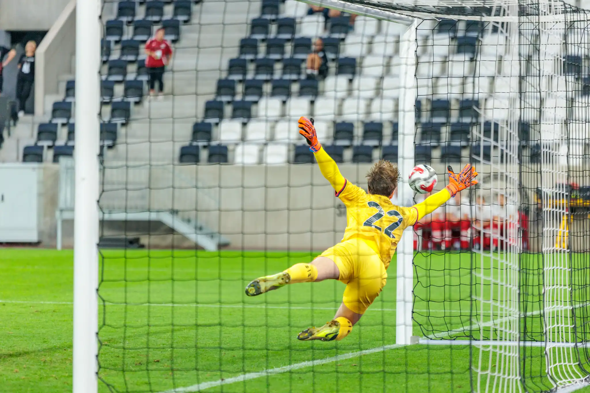 Ein Fußballtorhüter in gelbem Trikot mit der Nummer 22 pariert mit orangefarbenen Handschuhen einen Ball während eines spannenden Spiels der Nero Summer Series 