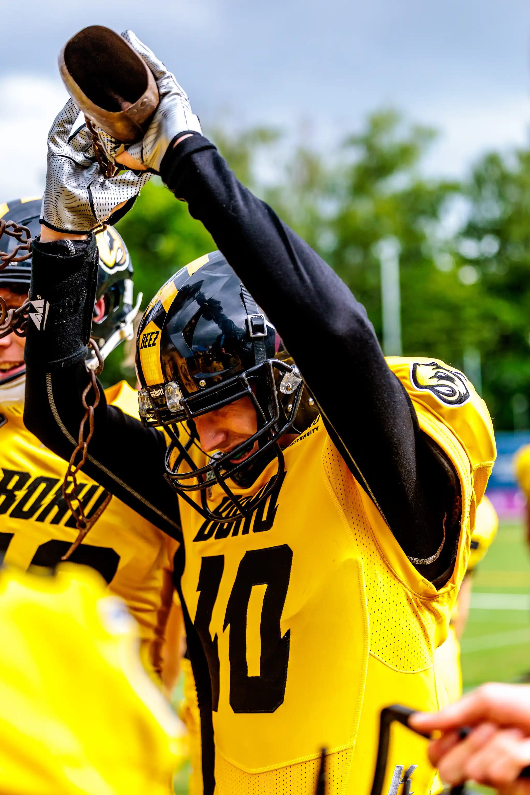 Ein American-Football-Spieler in gelb-schwarzer Uniform feiert mit einer großen Metallglocke über dem Kopf