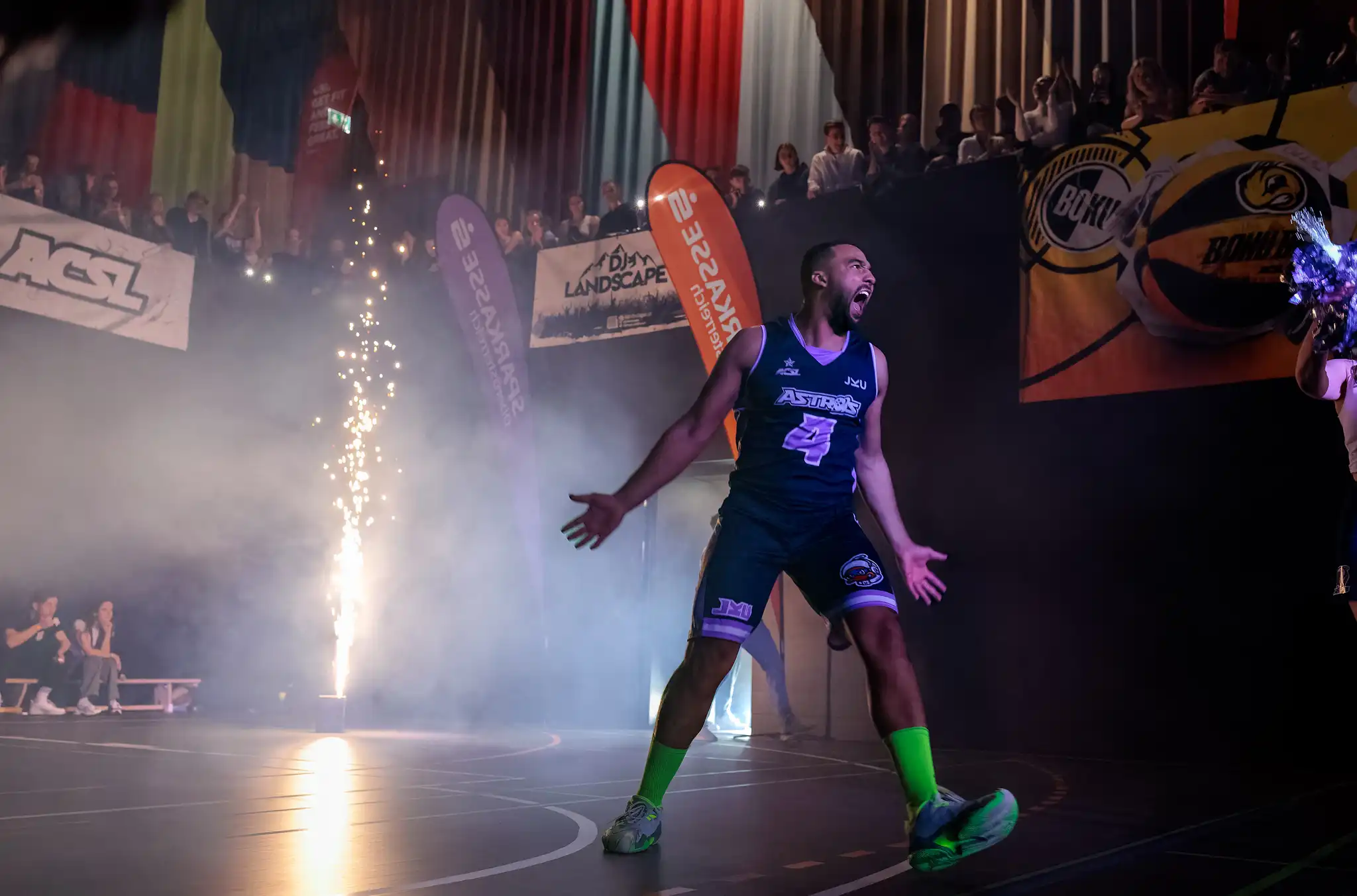 Ein emotionaler Basketballspieler der JKU Astros mit der Nummer 4 stürmt jubelnd unter Funkenregen auf das Spielfeld