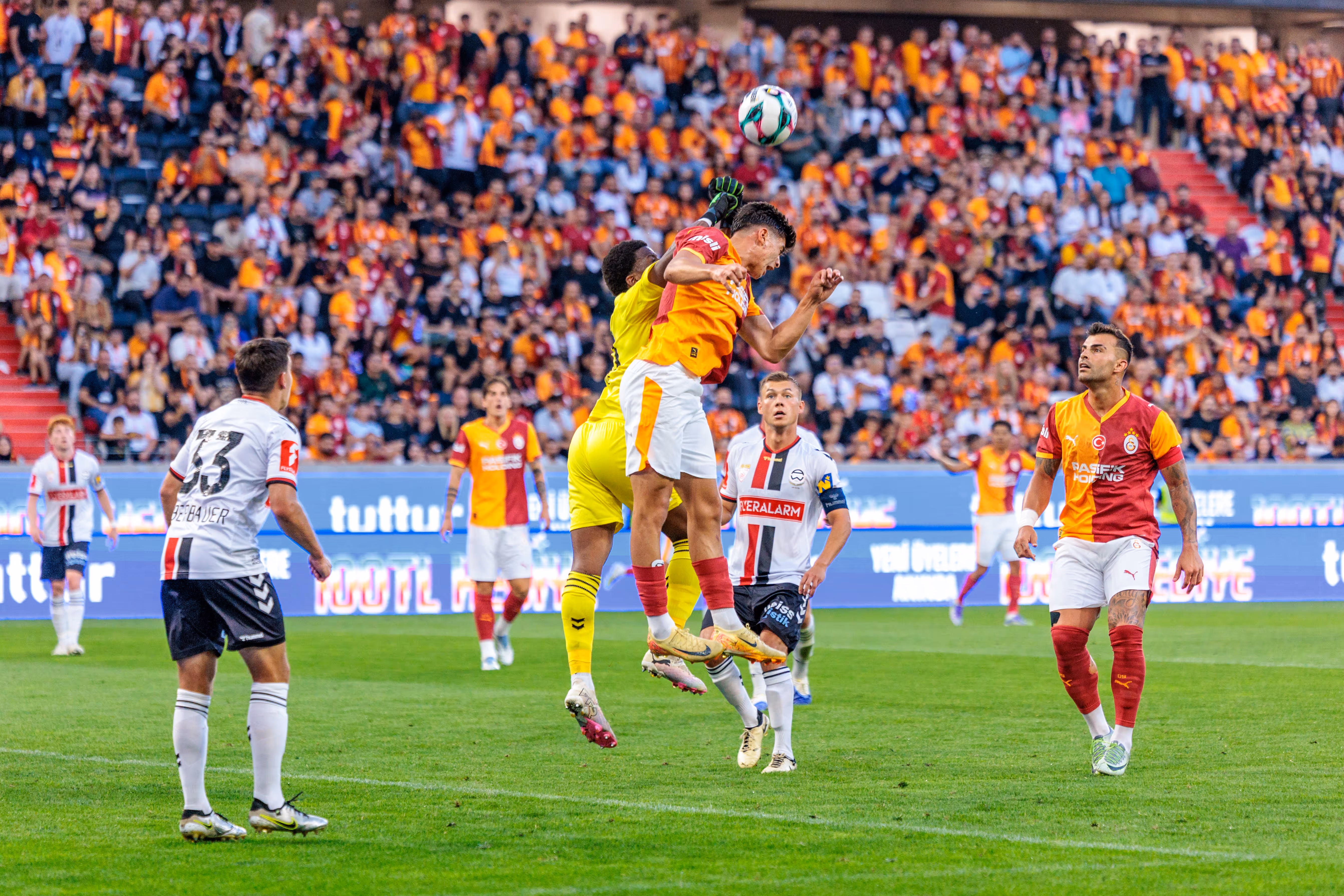 Spieler von Galatasaray und Admira Wacker duellieren sich bei einem Kopfball in der Luft während eines Fußballspiels der Nero Summer Series vor begeisterten Fans