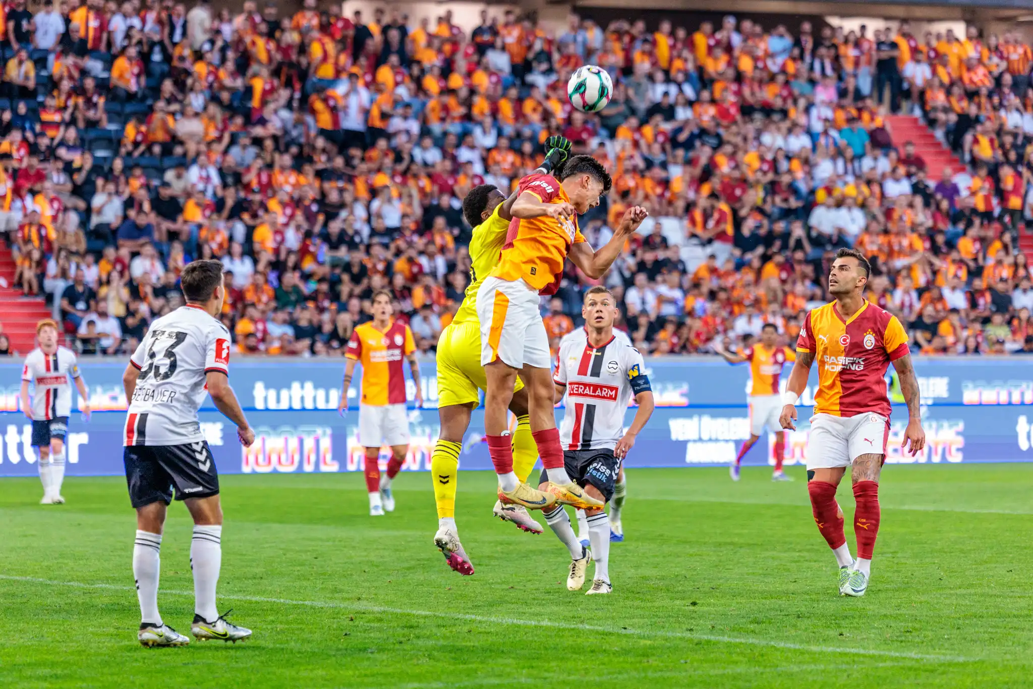 Spieler von Galatasaray und Admira Wacker duellieren sich bei einem Kopfball in der Luft während eines Fußballspiels der Nero Summer Series vor begeisterten Fans 