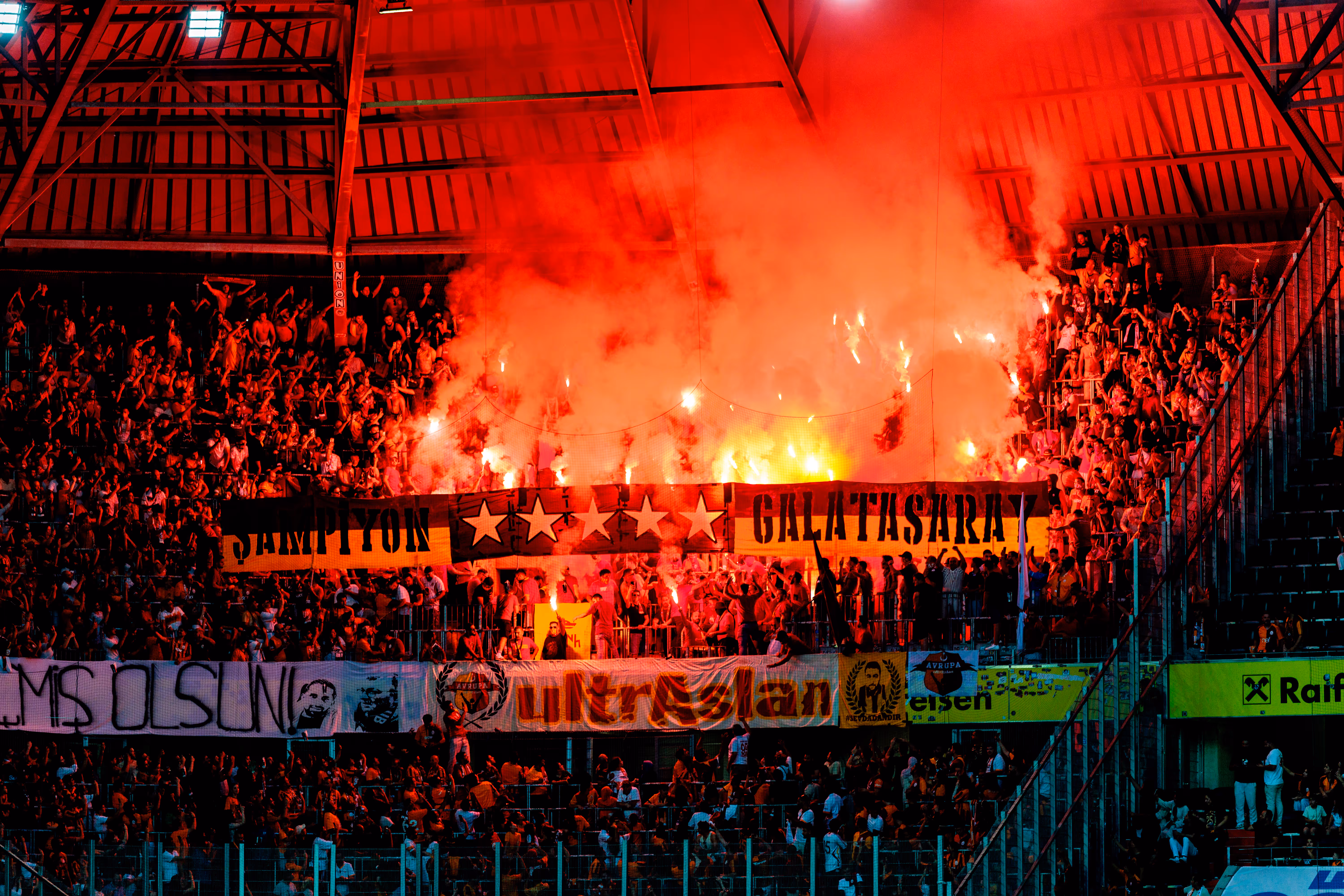 Galatasaray-Fans schaffen in einem Fußballstadion eine leidenschaftliche Atmosphäre mit zahlreichen roten Fackeln und aufsteigendem Rauch