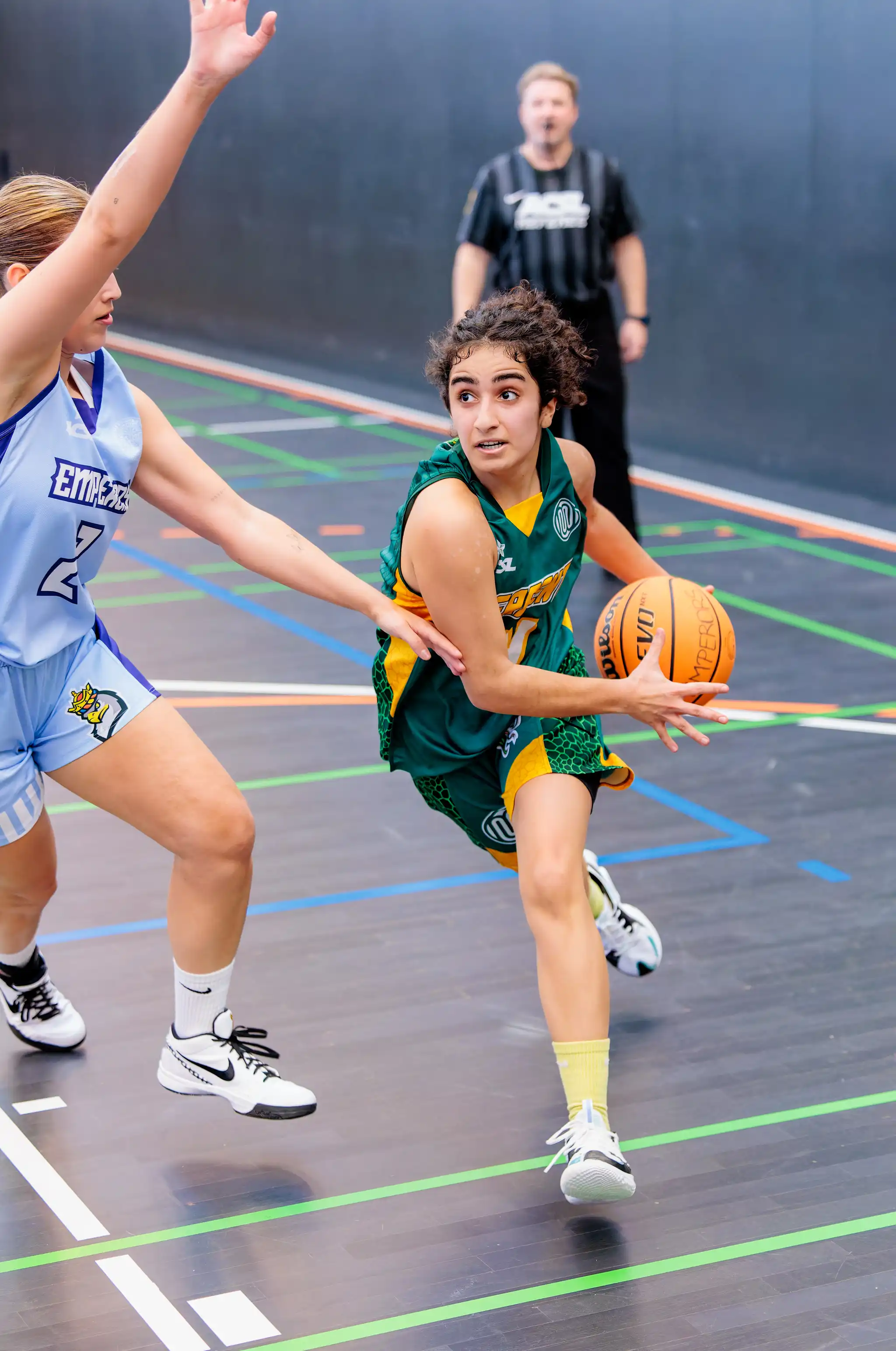 Eine Basketballspielerin im grünen Trikot dribbelt dynamisch den Ball, während eine Gegenspielerin im hellblauen Trikot verteidigt