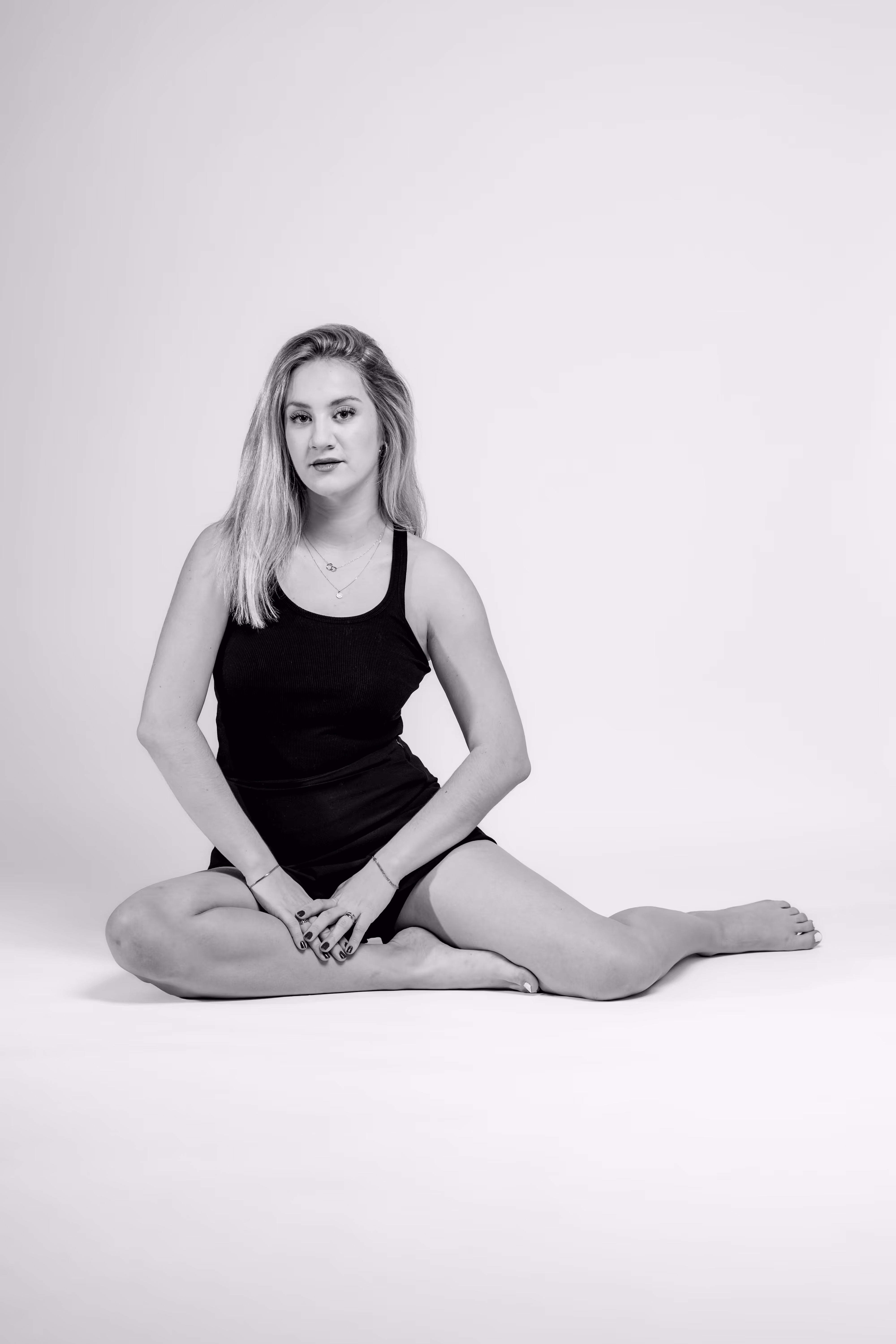 Model Anna sitzt in einem lässigen schwarzen Outfit in einer eleganten Pose auf dem weißen Boden eines Fotostudios und blickt direkt in die Kamera