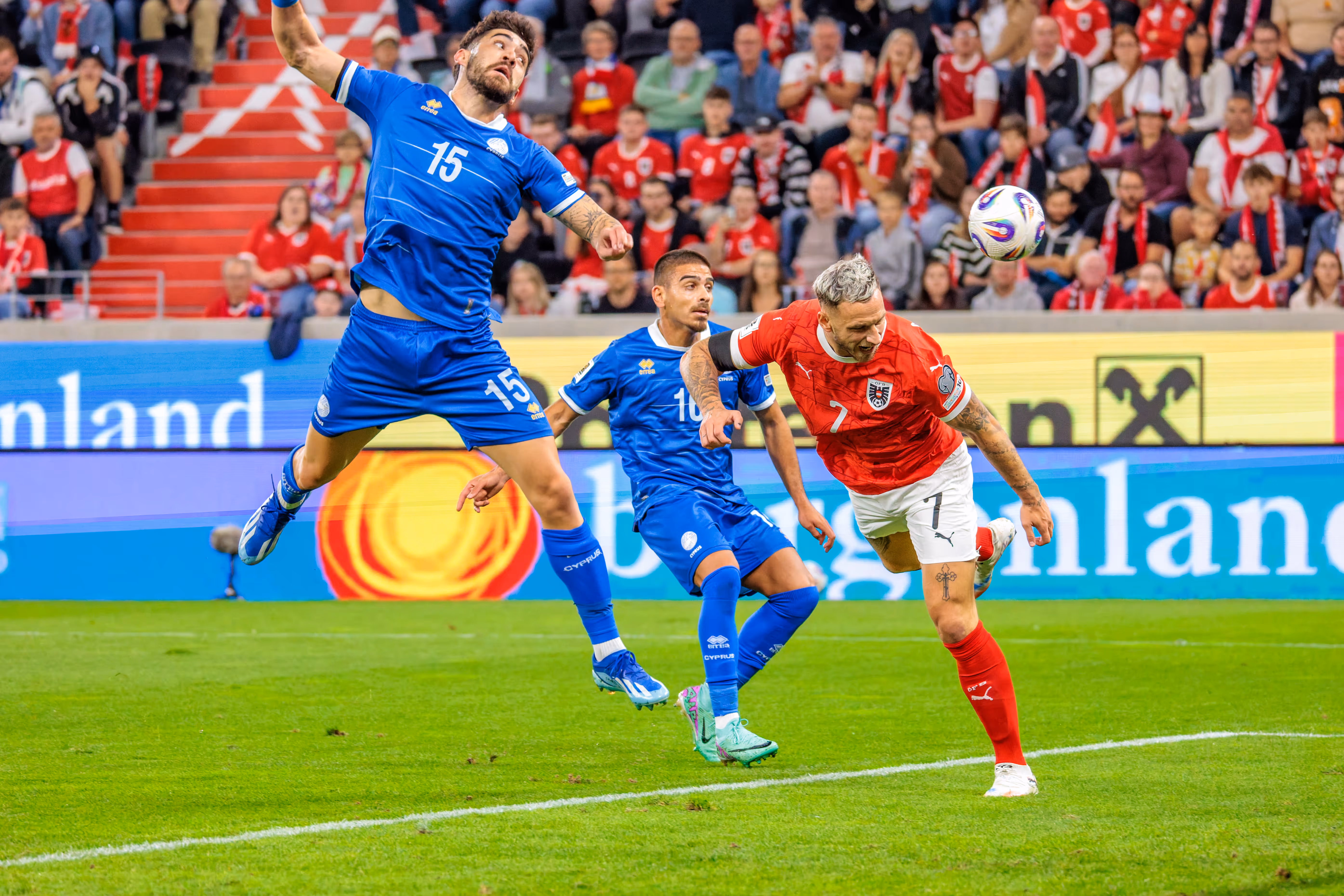Marko Arnautović im roten Trikot von Österreich und Christos Shelis im blauen Trikot von Zypern springen in einem Kopfballduell um den Fußball vor vollen Zuschauerrängen