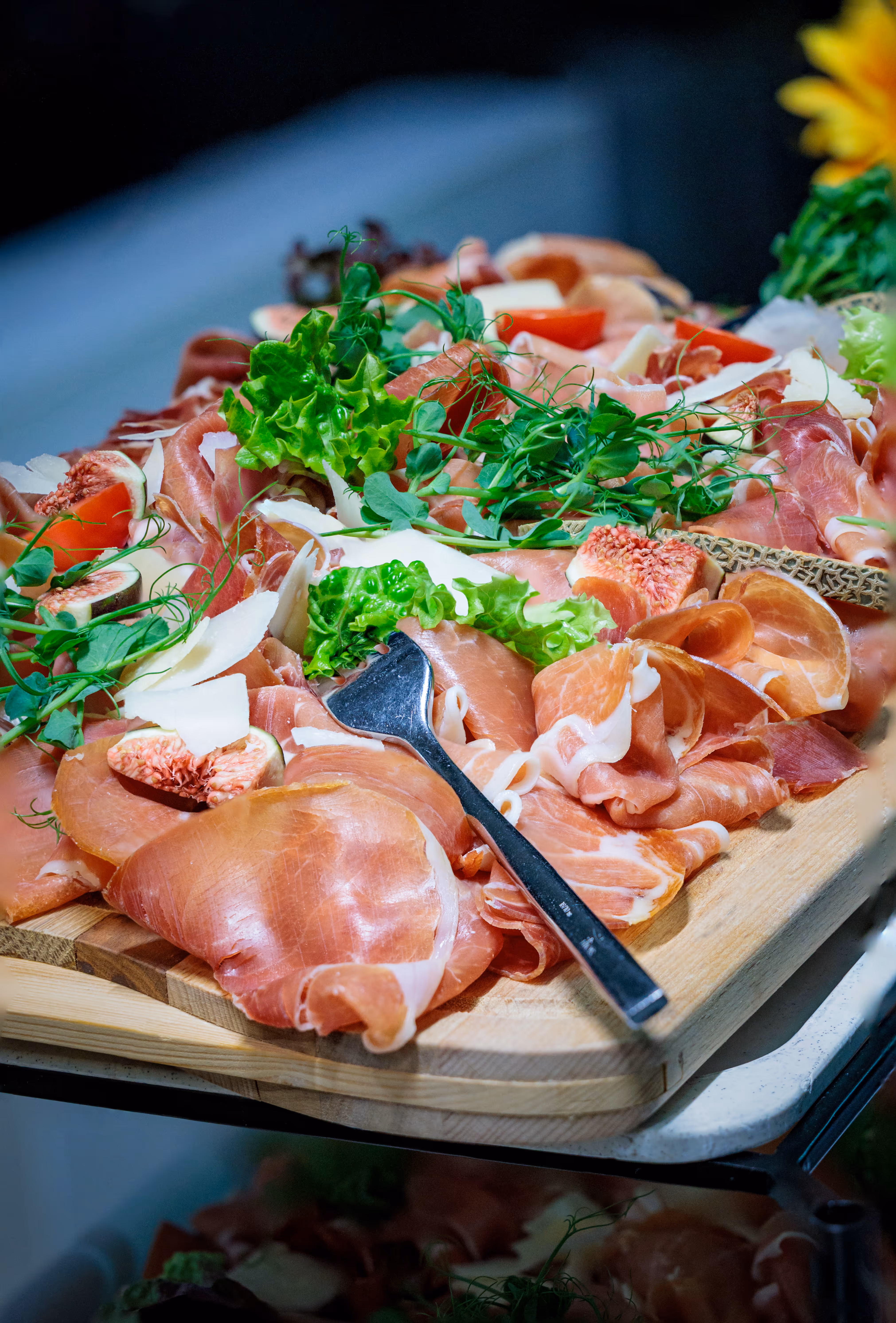 Eine rustikale Aufschnittplatte mit Prosciutto, frischen Feigen und Käsespänen, serviert auf einem Holzbrett im VIP-Bereich bei einem Spiel der Black Wings Linz