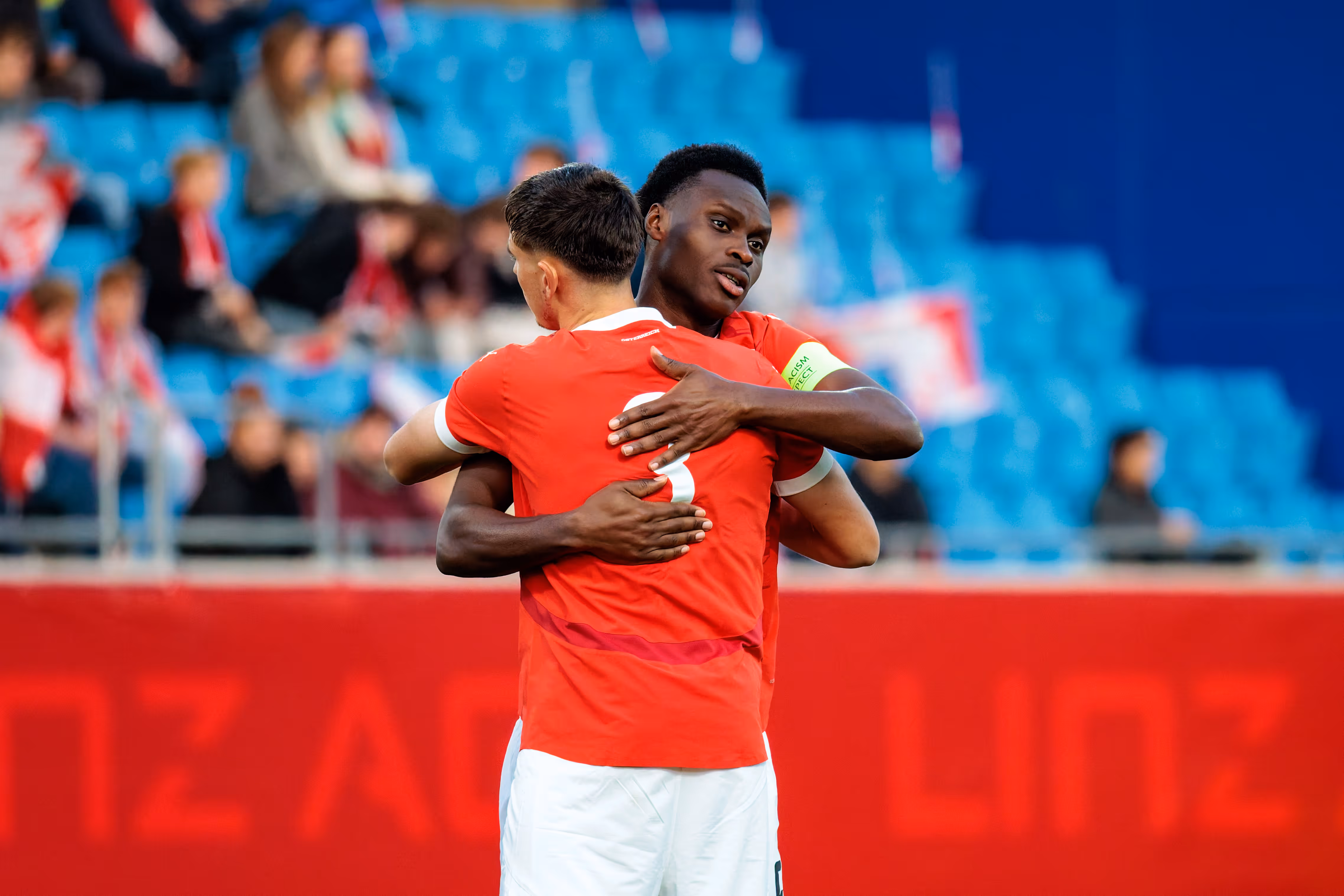 Zwei österreichische U21-Fußballspieler, Samson Baidoo und Tim Trummer, umarmen sich, wobei Baidoo die Kapitänsschleife am linken Arm trägt