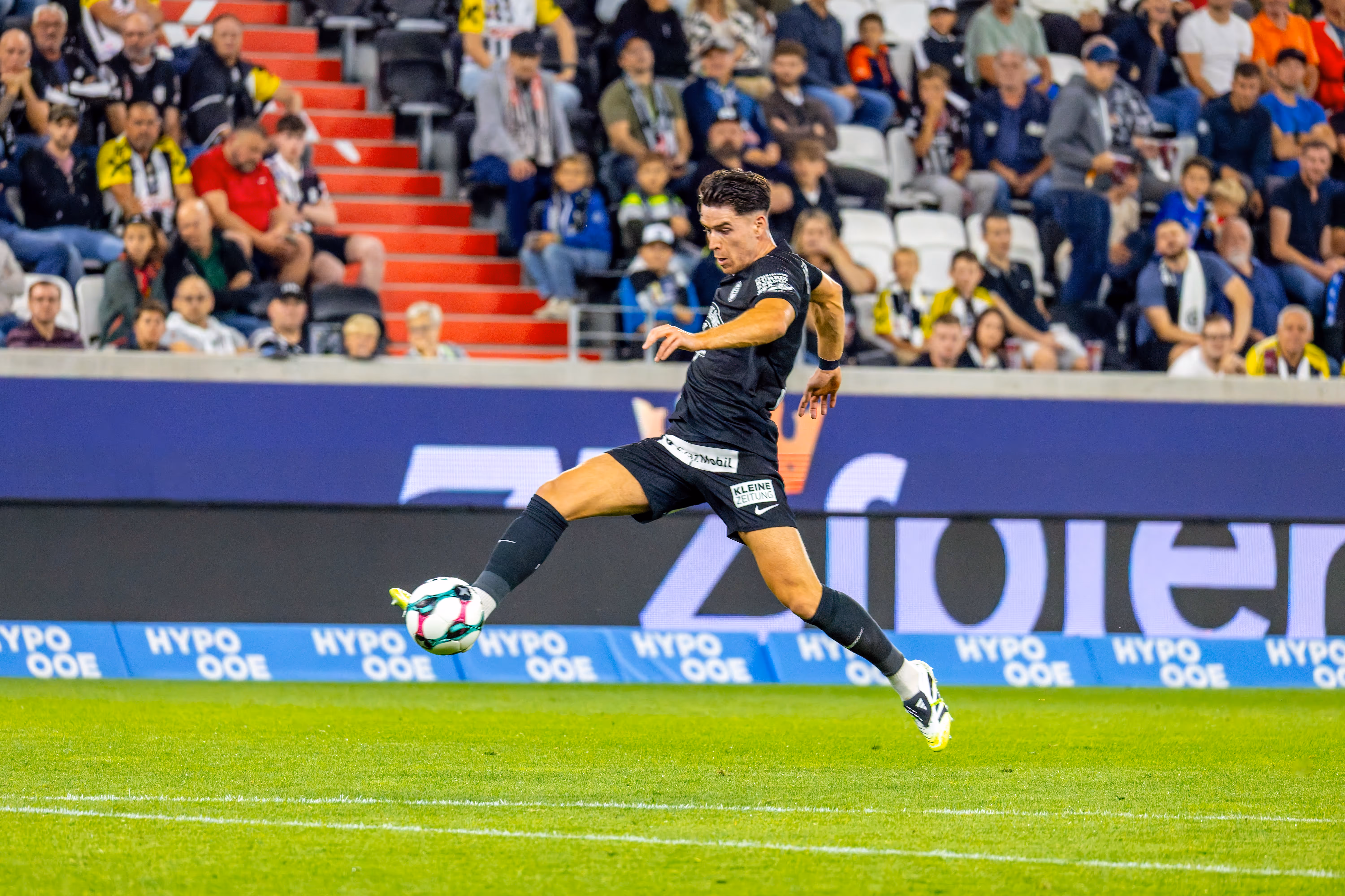 Ein Fußballspieler von Sturm Graz kontrolliert konzentriert einen Fußball auf dem grünen Spielfeld während eines Bundesligaspiels