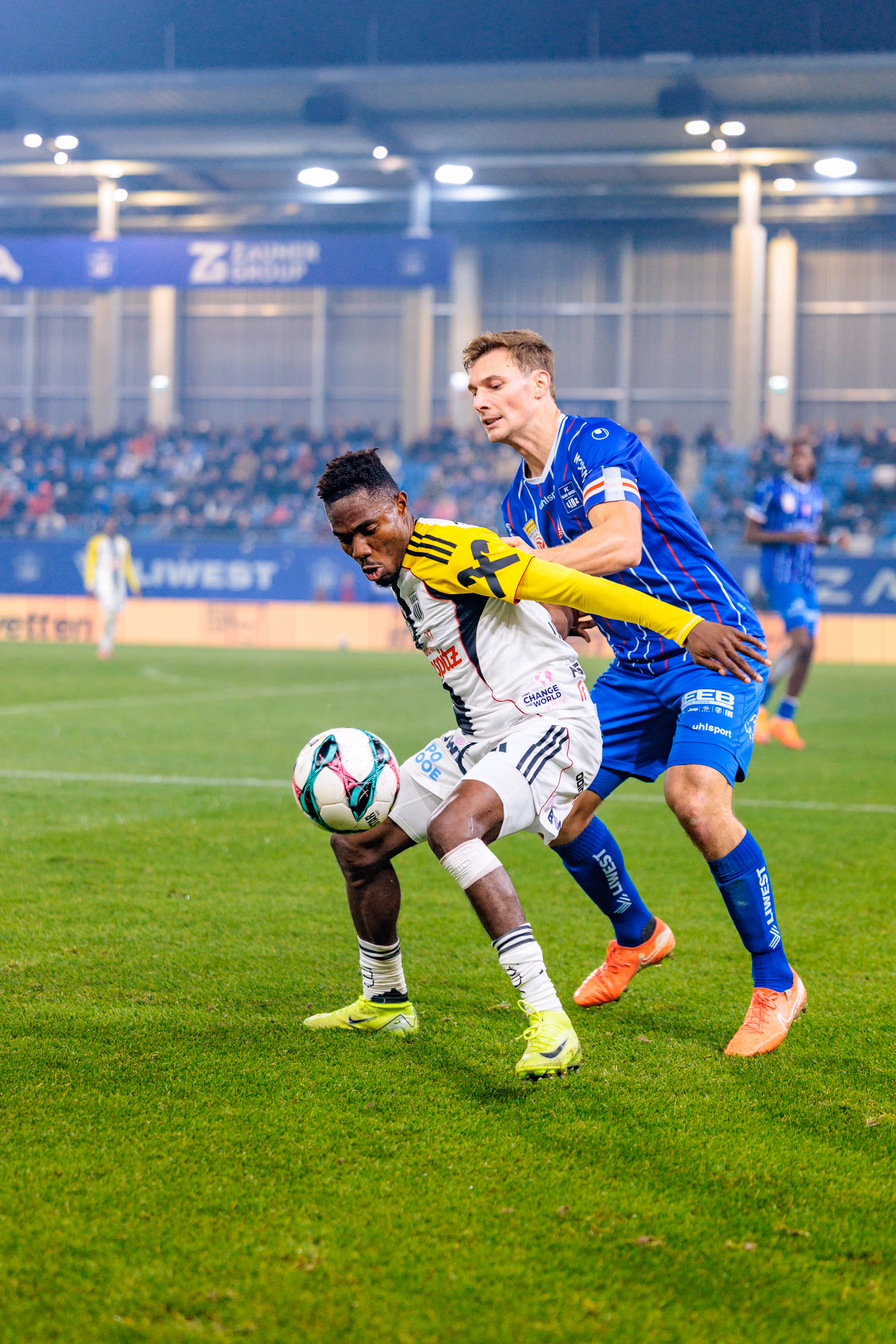 LASK-Spieler George Bello behauptet den Ball in einem intensiven Zweikampf gegen einen Spieler von Blau-Weiß Linz während des Linzer Derbys