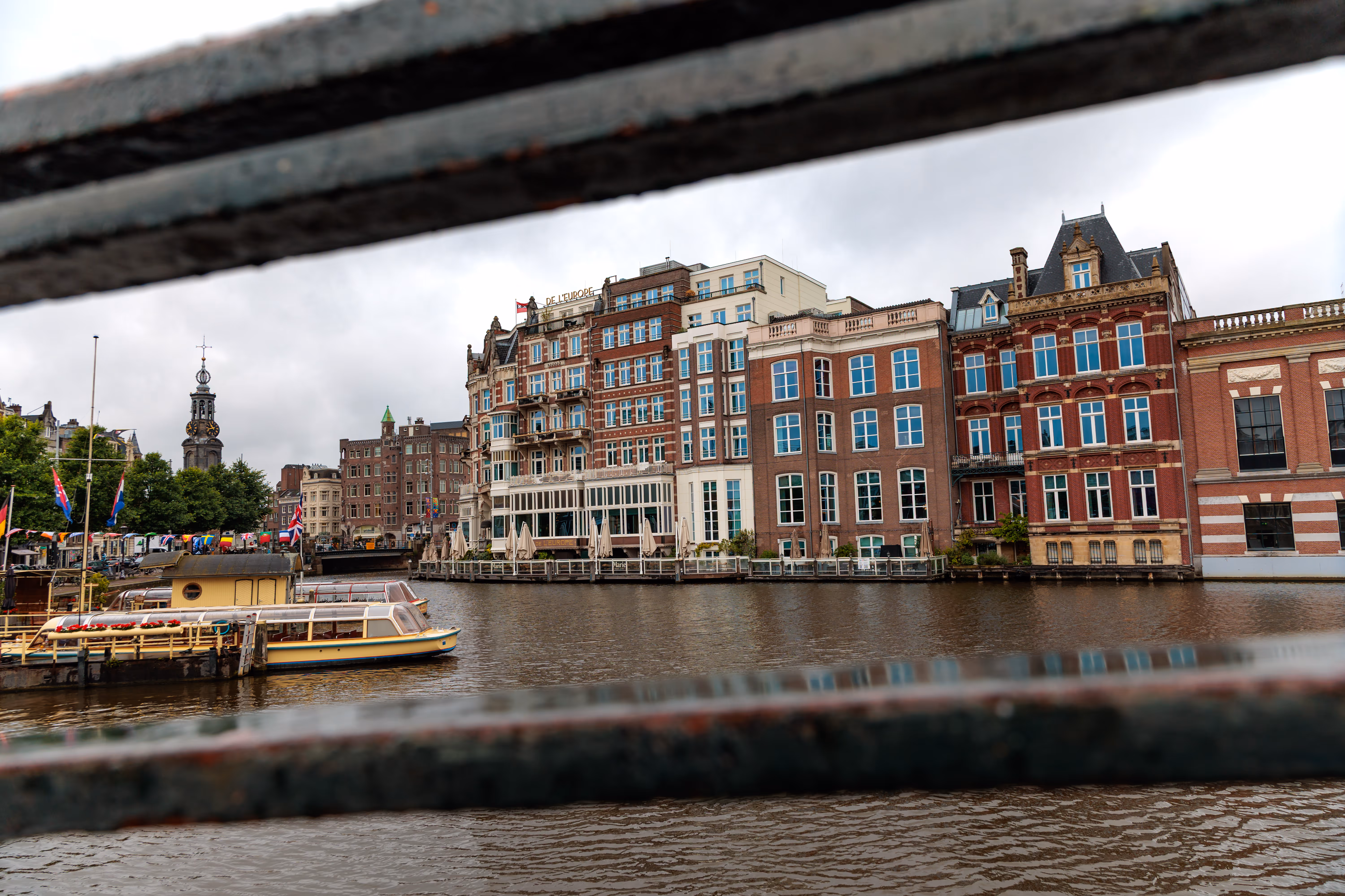 Historische Backsteinhäuser säumen einen Amsterdamer Kanal mit Booten und einem Kirchturm bei wolkigem Wetter