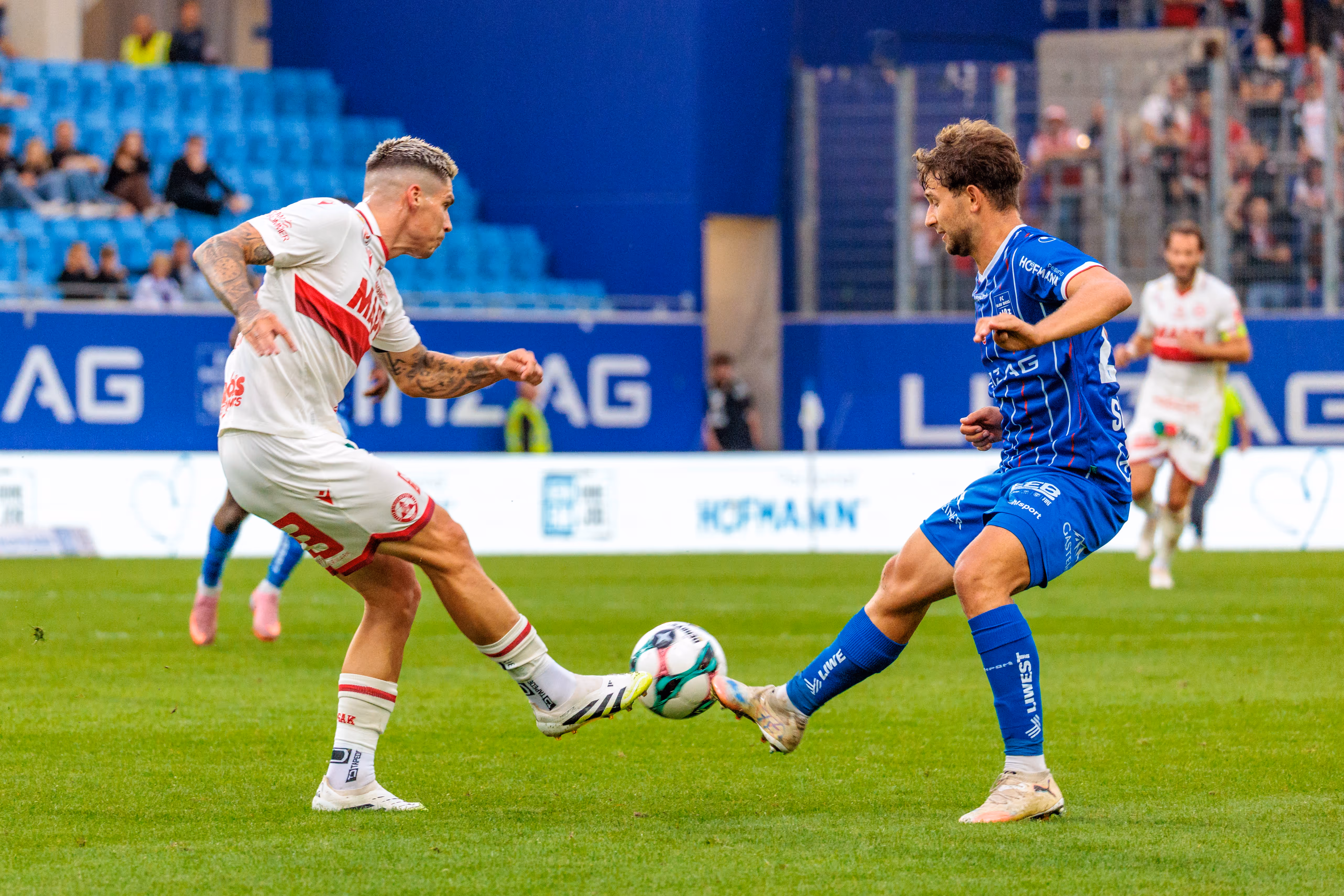 Zwei Fußballspieler, Alexander Briedl von Blau-Weiß Linz in blauem Trikot und Tio Cipot vom GAK in weißem Trikot, kämpfen während eines Ligaspiels um den Ball