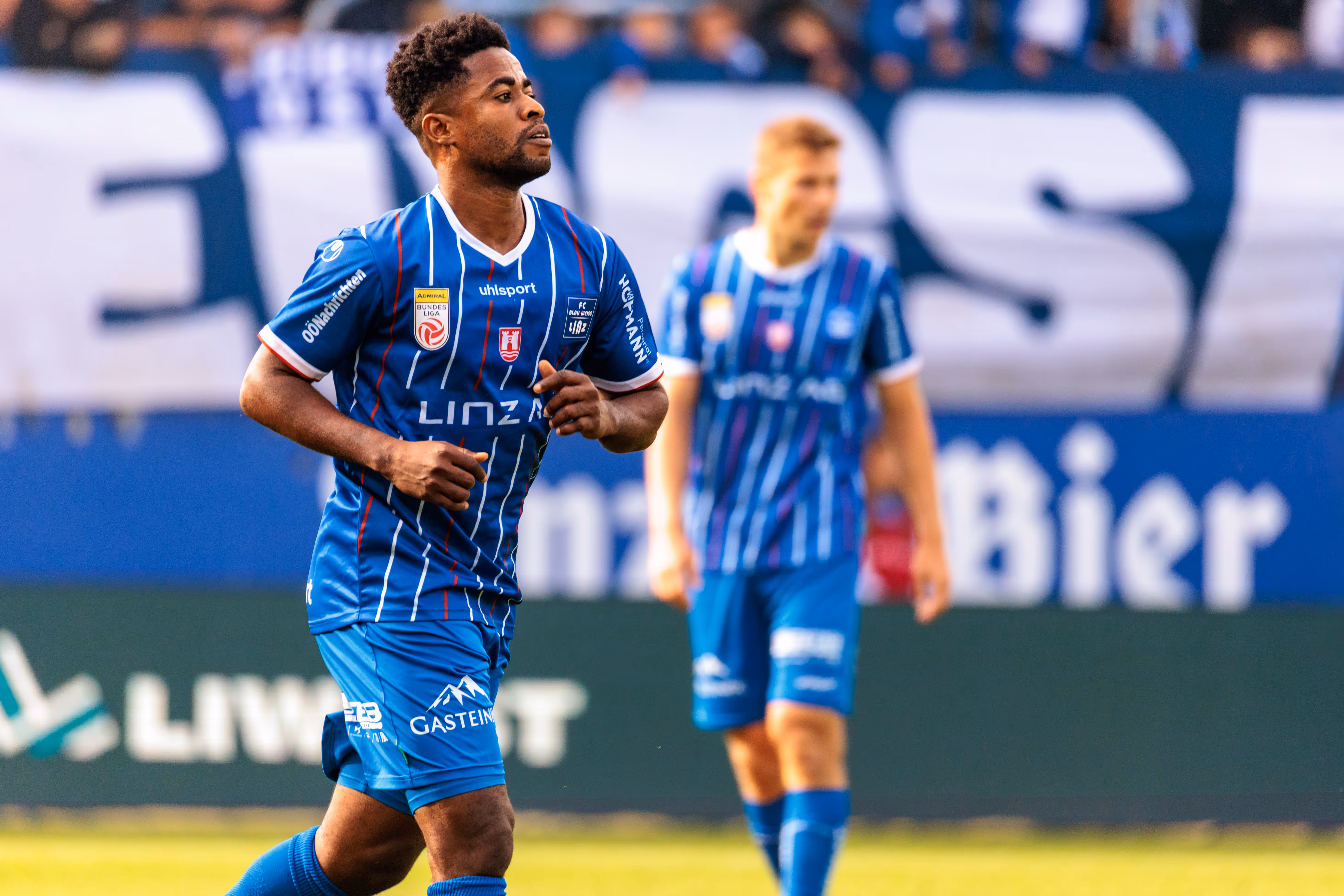 Ein dunkelhäutiger Fußballspieler des FC Blau-Weiß Linz mit Bart läuft im blau-weiß gestreiften Trikot konzentriert während eines Bundesligaspiels