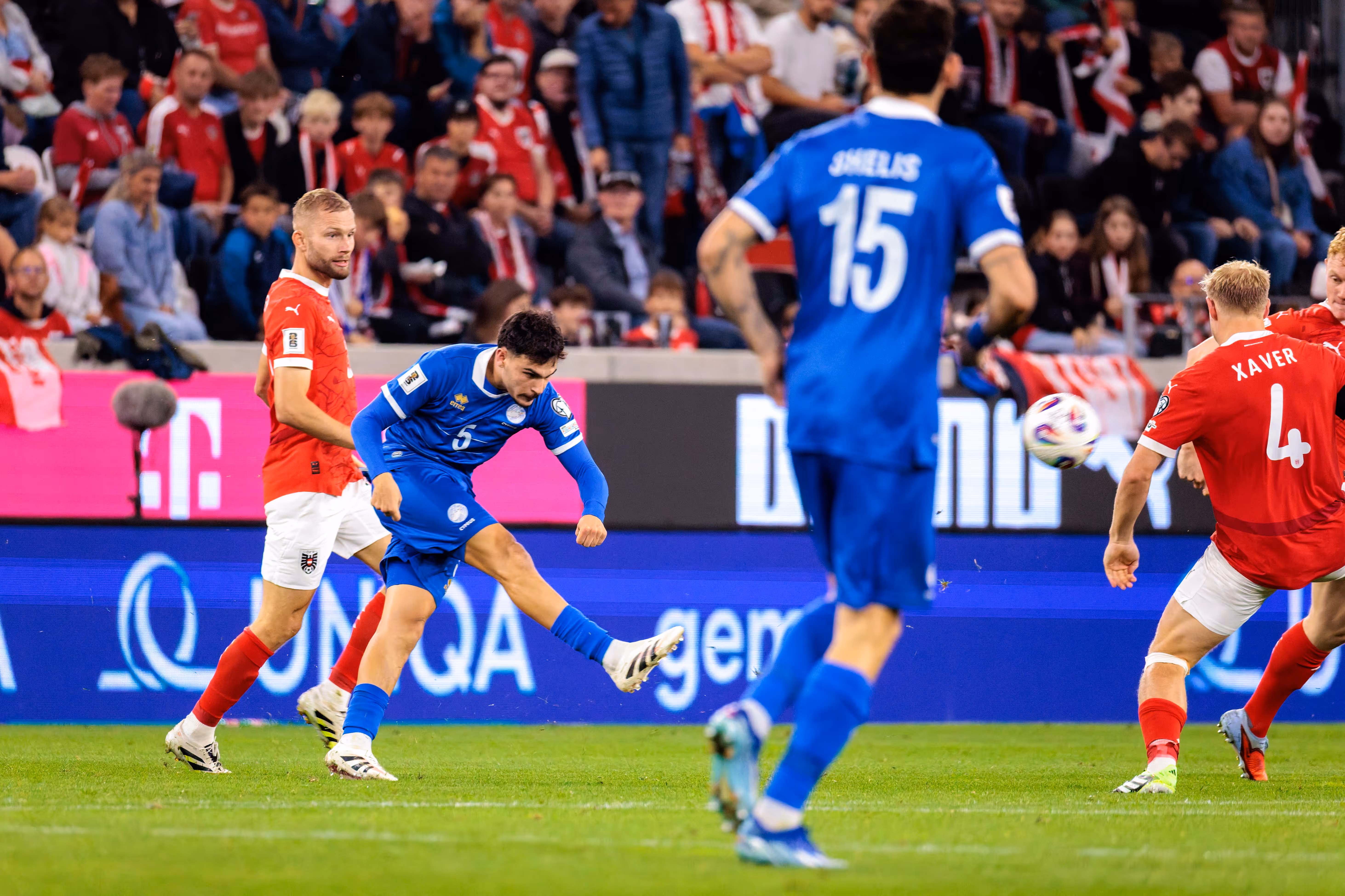 Der zypriotische Spieler Charalampos Charalampous (Nummer 5) schießt den Ball während eines WM-Qualifikationsspiels, während Xaver Schlager (Nummer 4) und Christoph Baumgartner (Nummer 19) von Österreich verteidigen