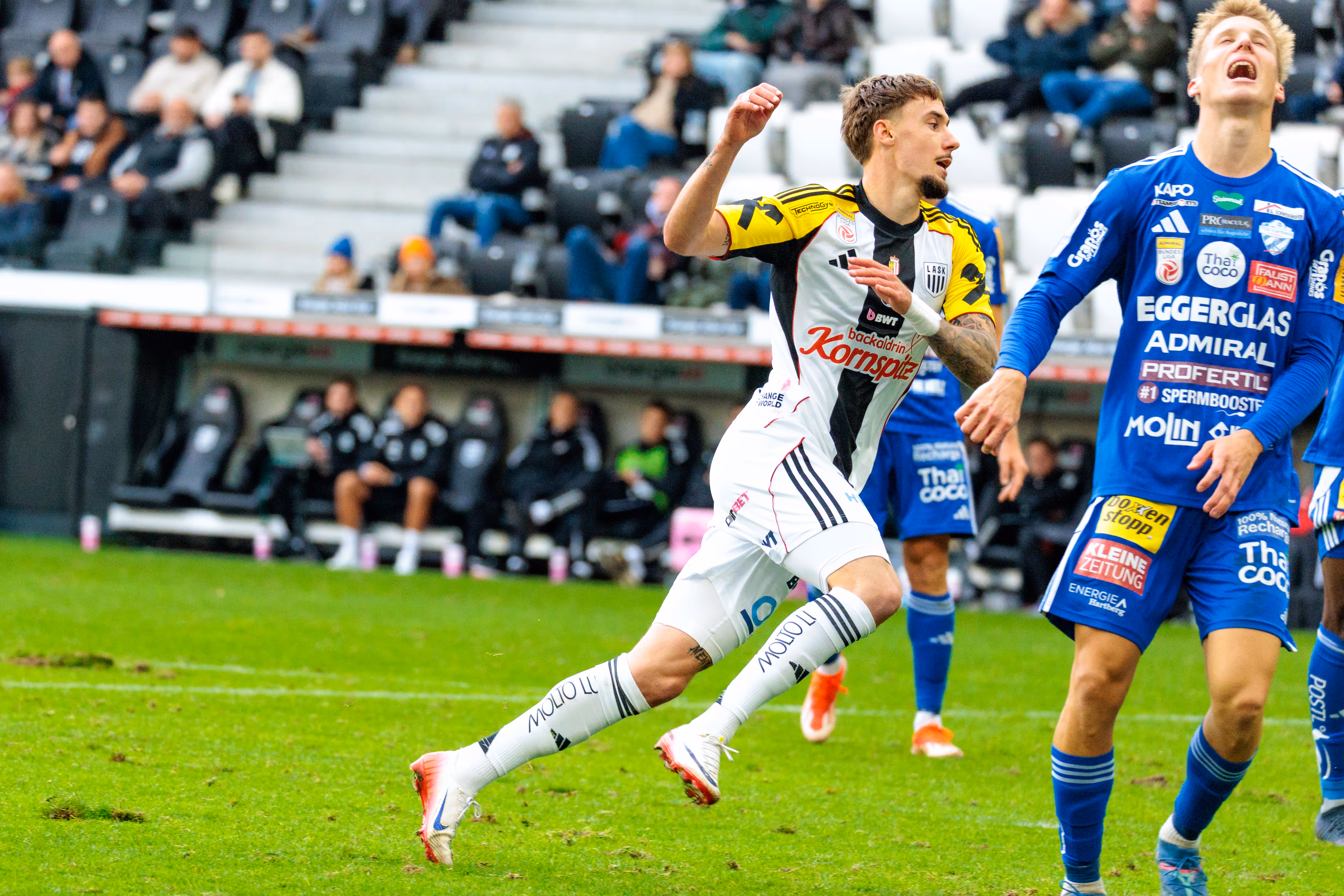 LASK-Spieler Christoph Lang feiert jubelnd seinen Treffer, während ein Gegenspieler vom TSV Hartberg im Hintergrund enttäuscht in den Himmel blickt
