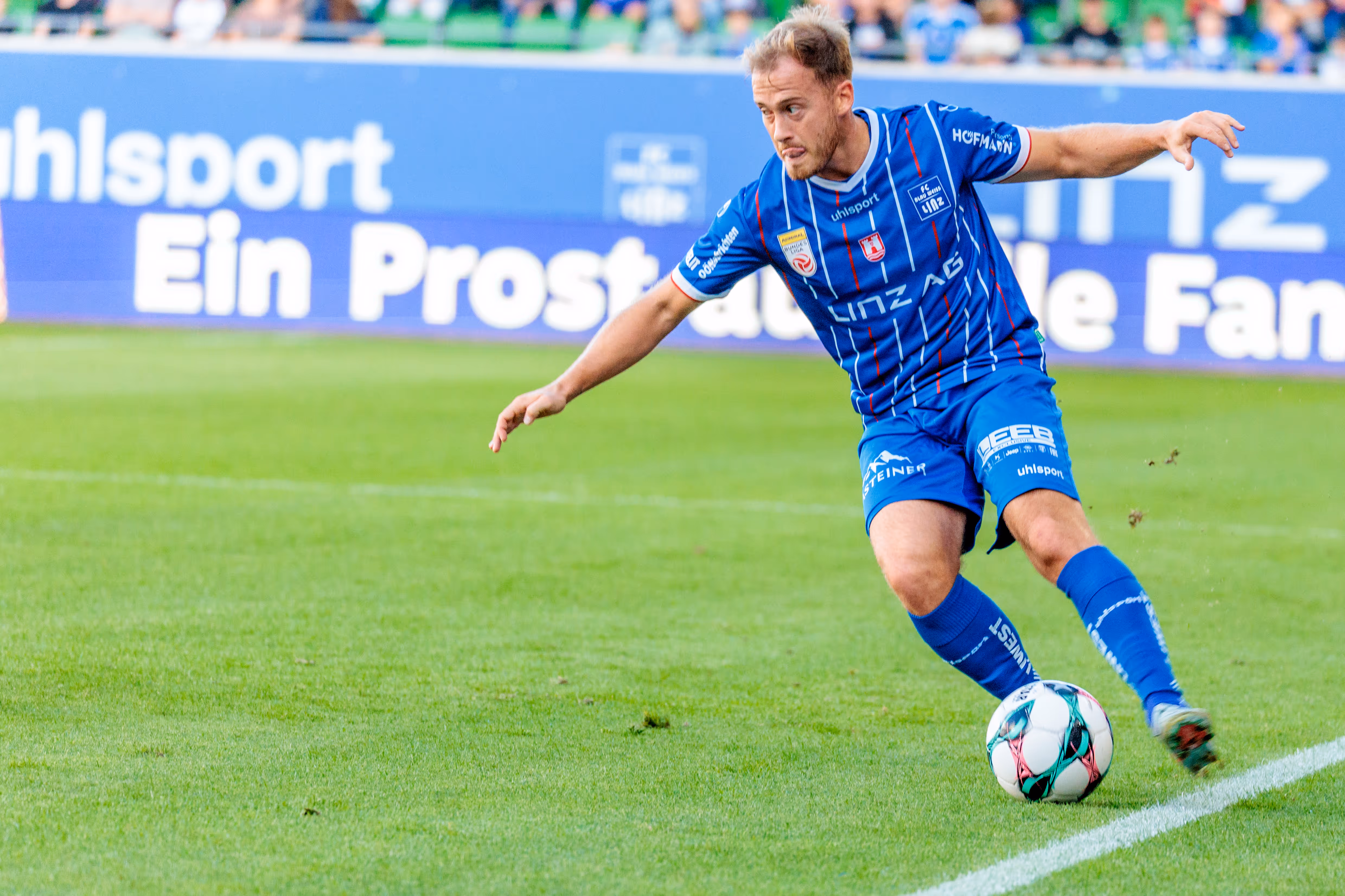 Dominik Reiter im blau-weißen Trikot von Blau-Weiß Linz dribbelt den Fußball mit konzentriertem Blick während eines Spiels