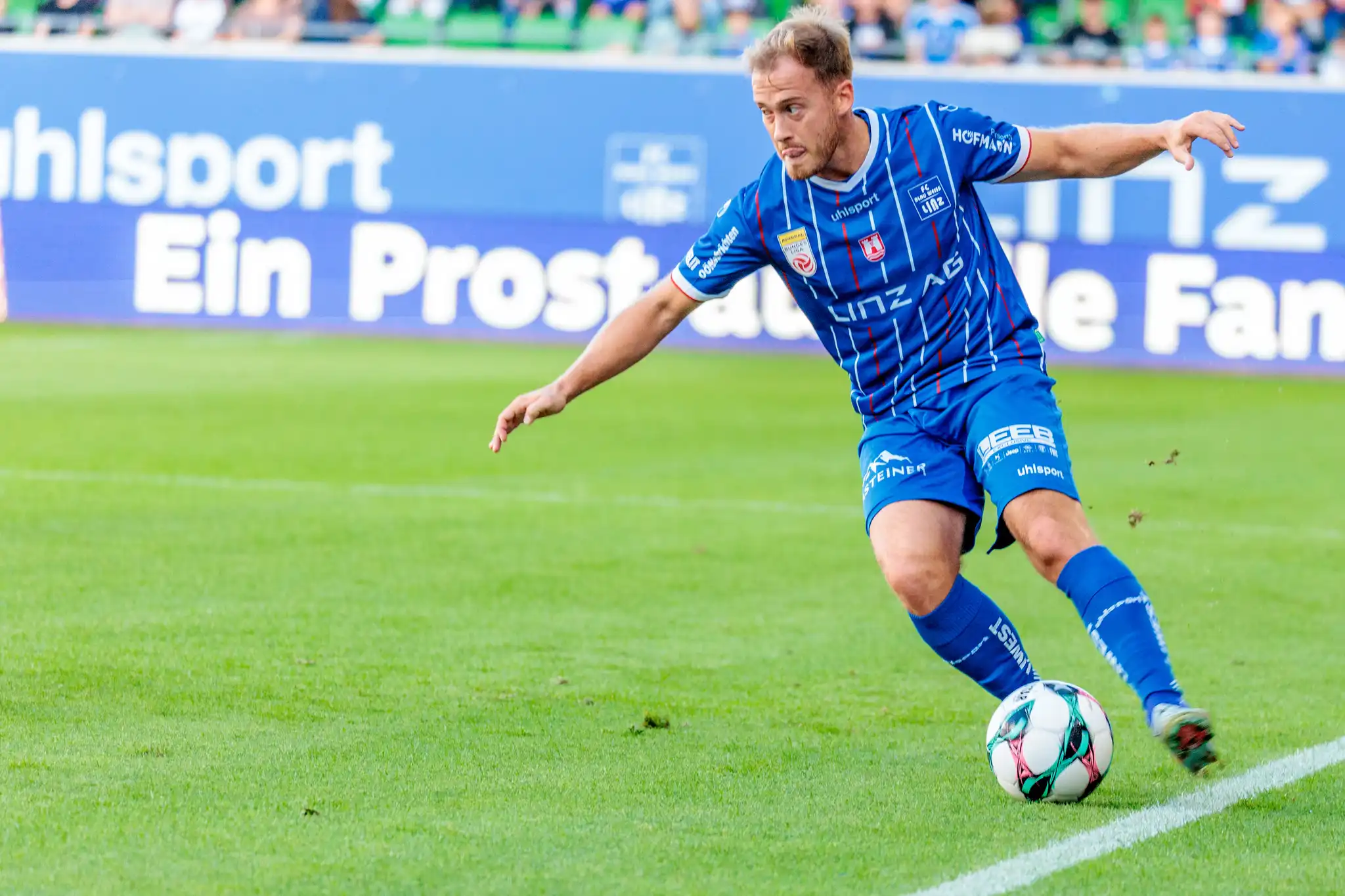 Dominik Reiter im blau-weißen Trikot von Blau-Weiß Linz dribbelt den Fußball mit konzentriertem Blick während eines Spiels