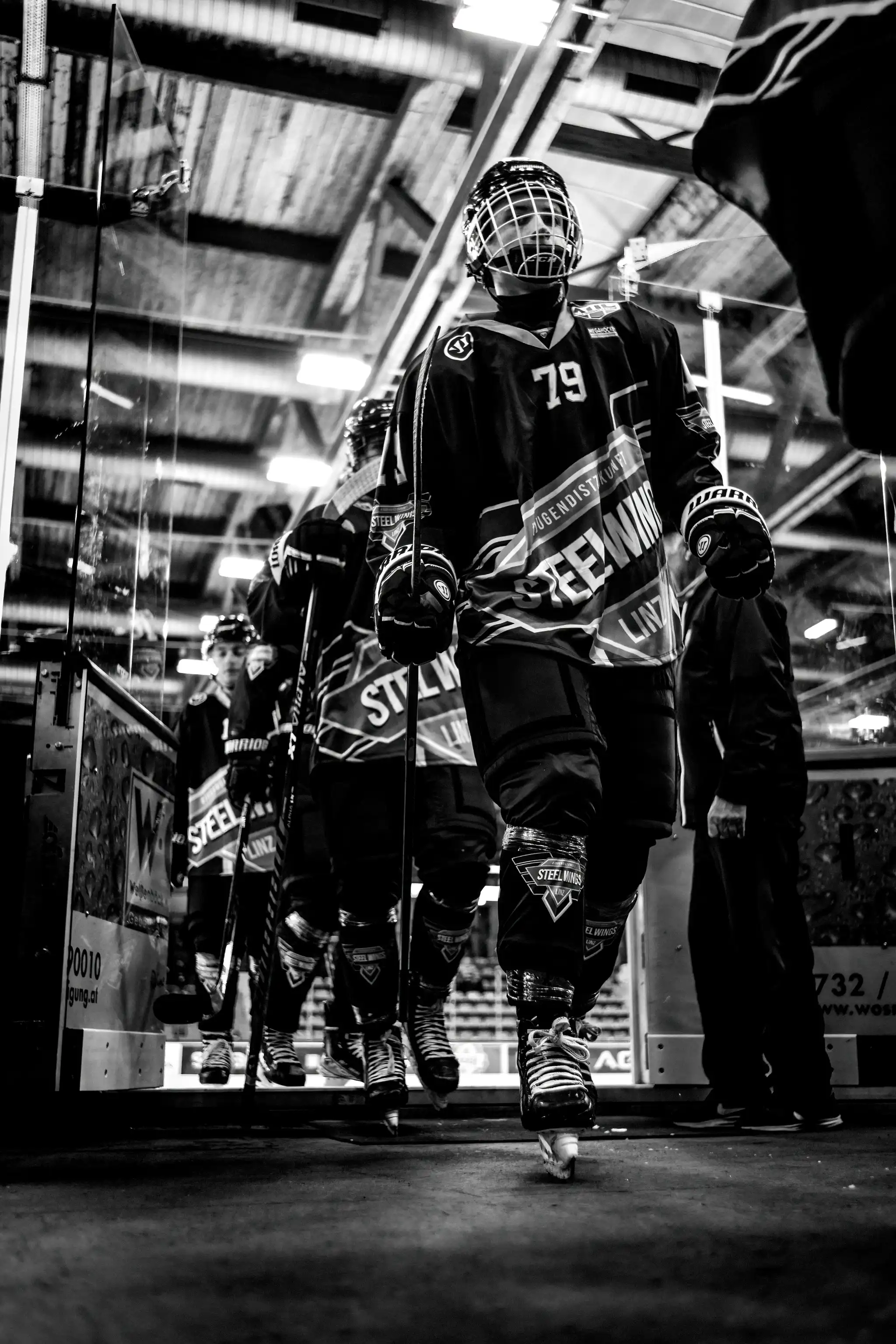 Eishockeyspieler der Steelwings Linz verlassen in einer dramatischen Schwarz-Weiß-Aufnahme das Eis ihrer Heimaarena 