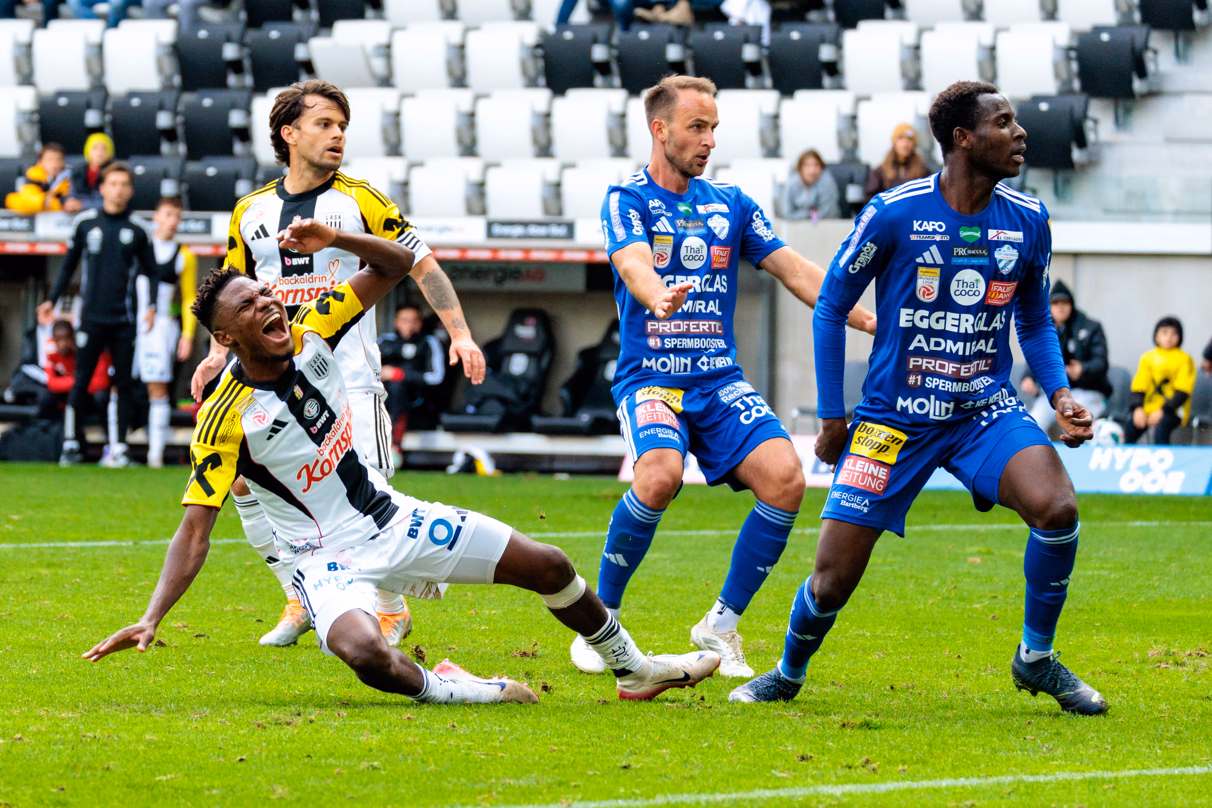 LASK-Spieler Moses Usor stürzt während eines intensiven Zweikampfs mit Hartberger Spielern emotional schreiend zu Boden