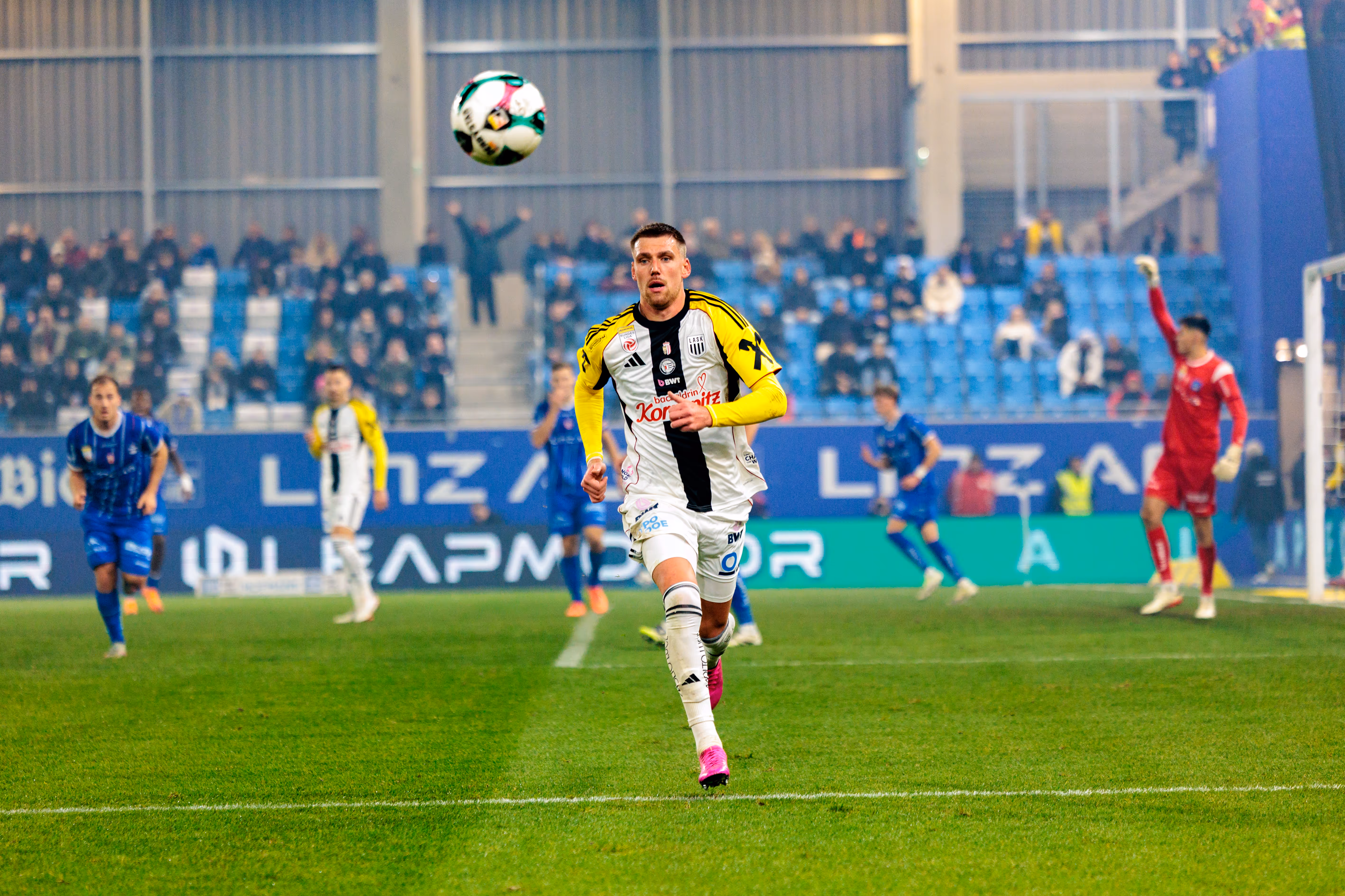 Der LASK-Spieler Florian Flecker in dynamischer Laufpose während des Linzer Derbys, der Fußball schwebt über ihm in der Luft