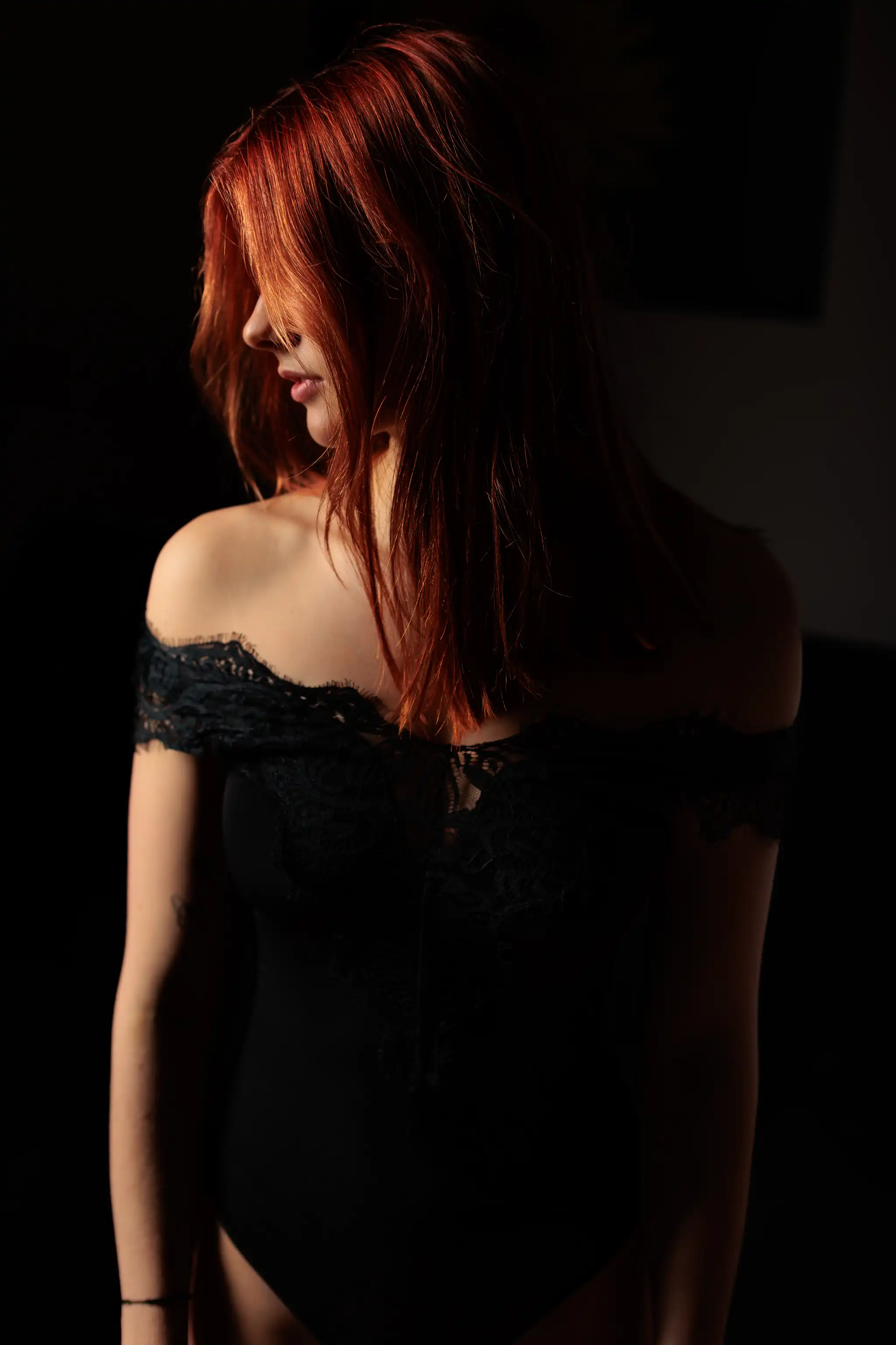 Geheimnisvolles Profil-Portrait von Sarah mit leuchtend roten Haaren in einem eleganten schwarzen Spitzen-Body bei stimmungsvoller Lichtsetzung