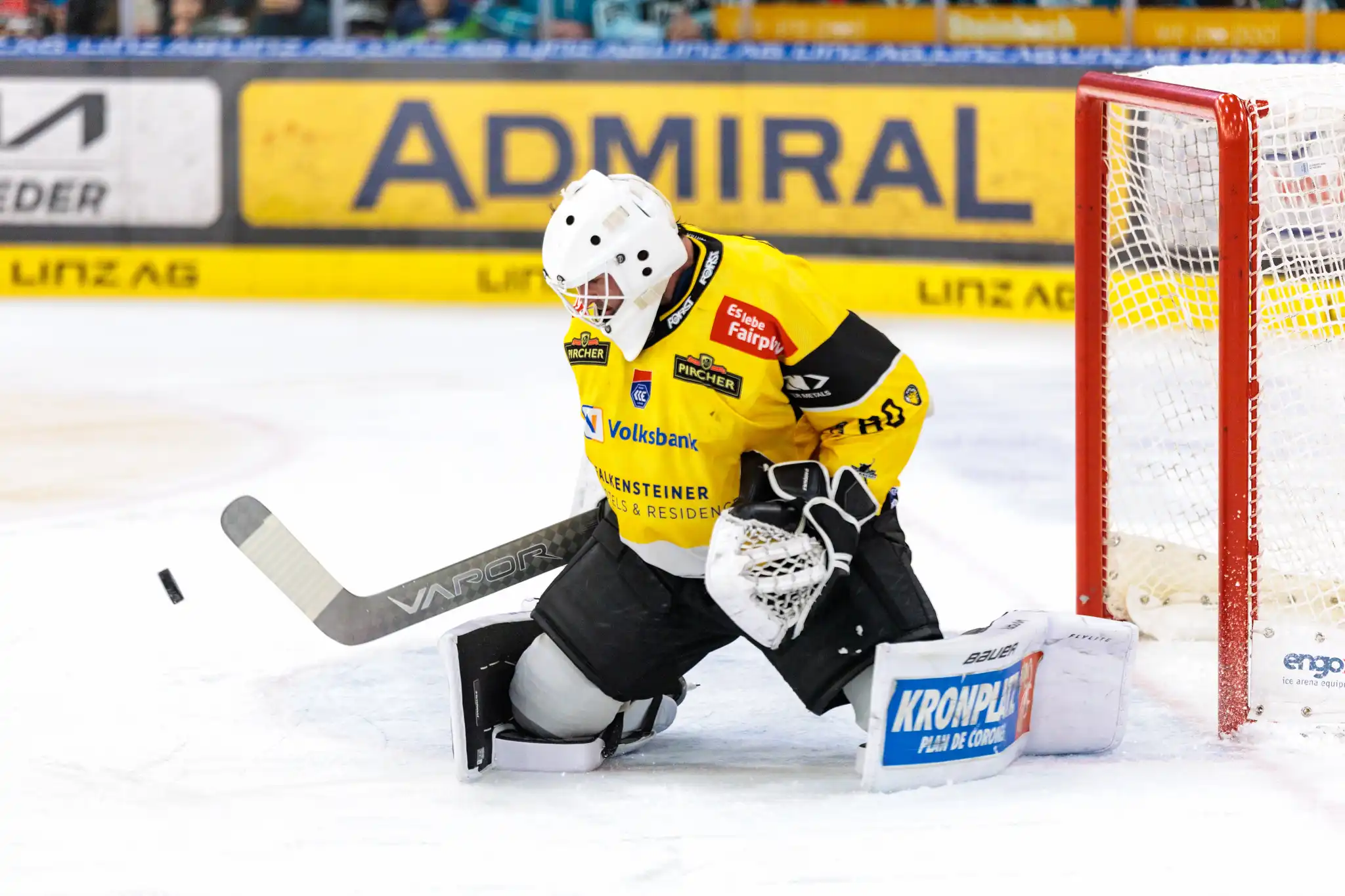 Der Torhüter des HC Pustertal, Edward Pasquale, in seiner gelb-schwarzen Ausrüstung bei einer Parade auf den Knien, während der Puck links von ihm durch die Luft fliegt