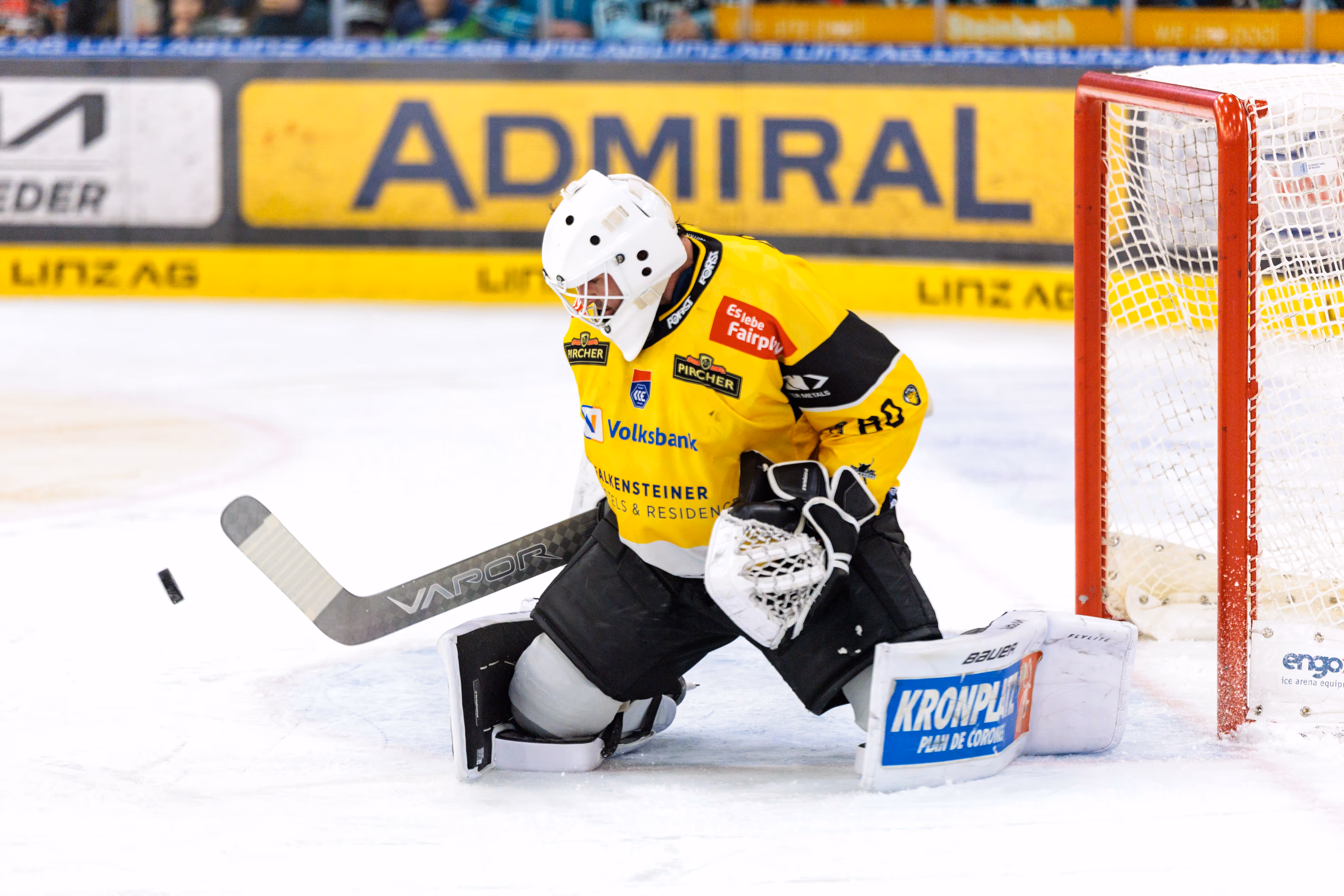 Der Torhüter des HC Pustertal, Edward Pasquale, in seiner gelb-schwarzen Ausrüstung bei einer Parade auf den Knien, während der Puck links von ihm durch die Luft fliegt
