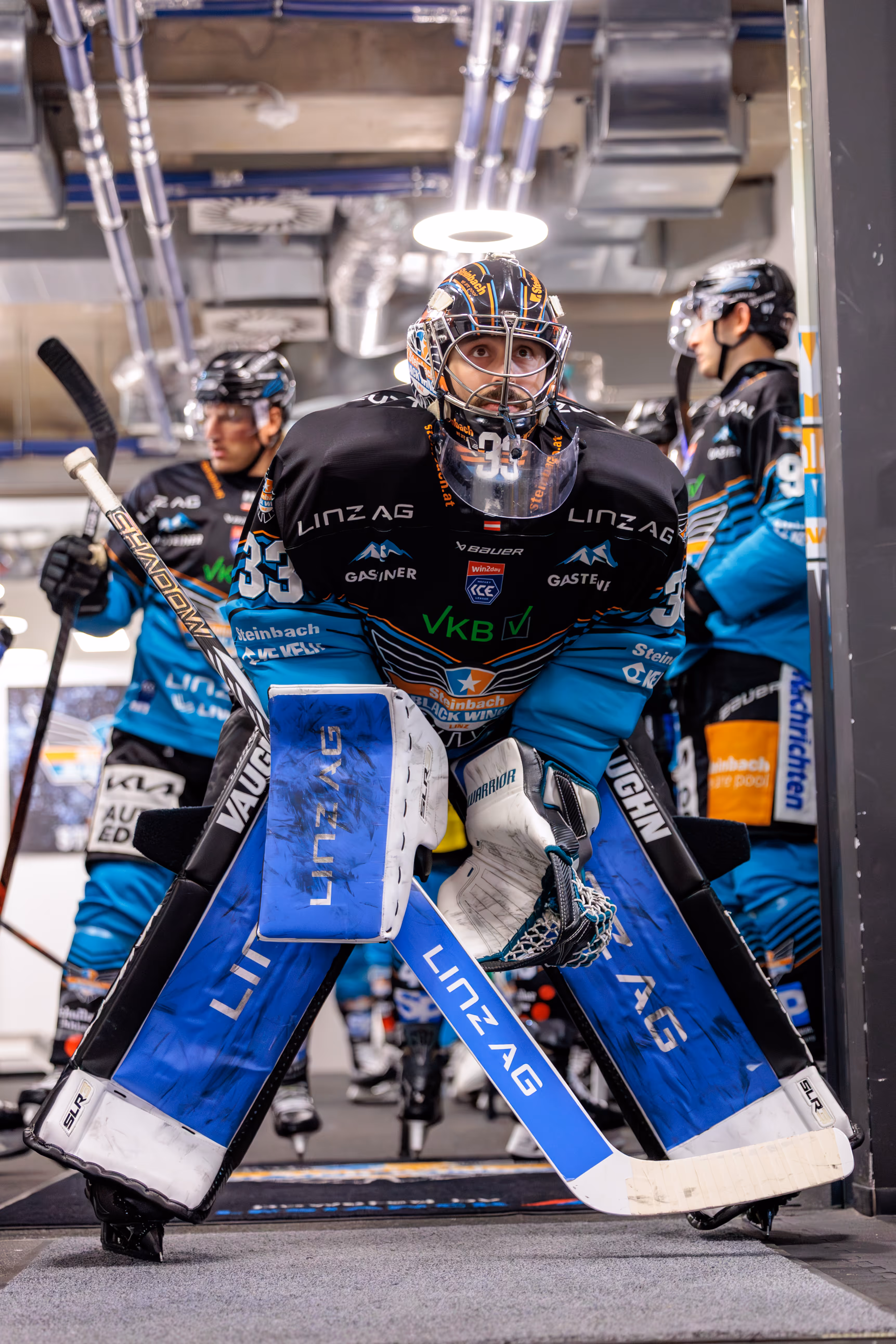 Der Eishockey-Goalie Thomas Höneckl von den Steinbach Black Wings Linz blickt in voller Montur und mit einem leuchtenden Ring über dem Helm konzentriert aus dem Spielertunnel