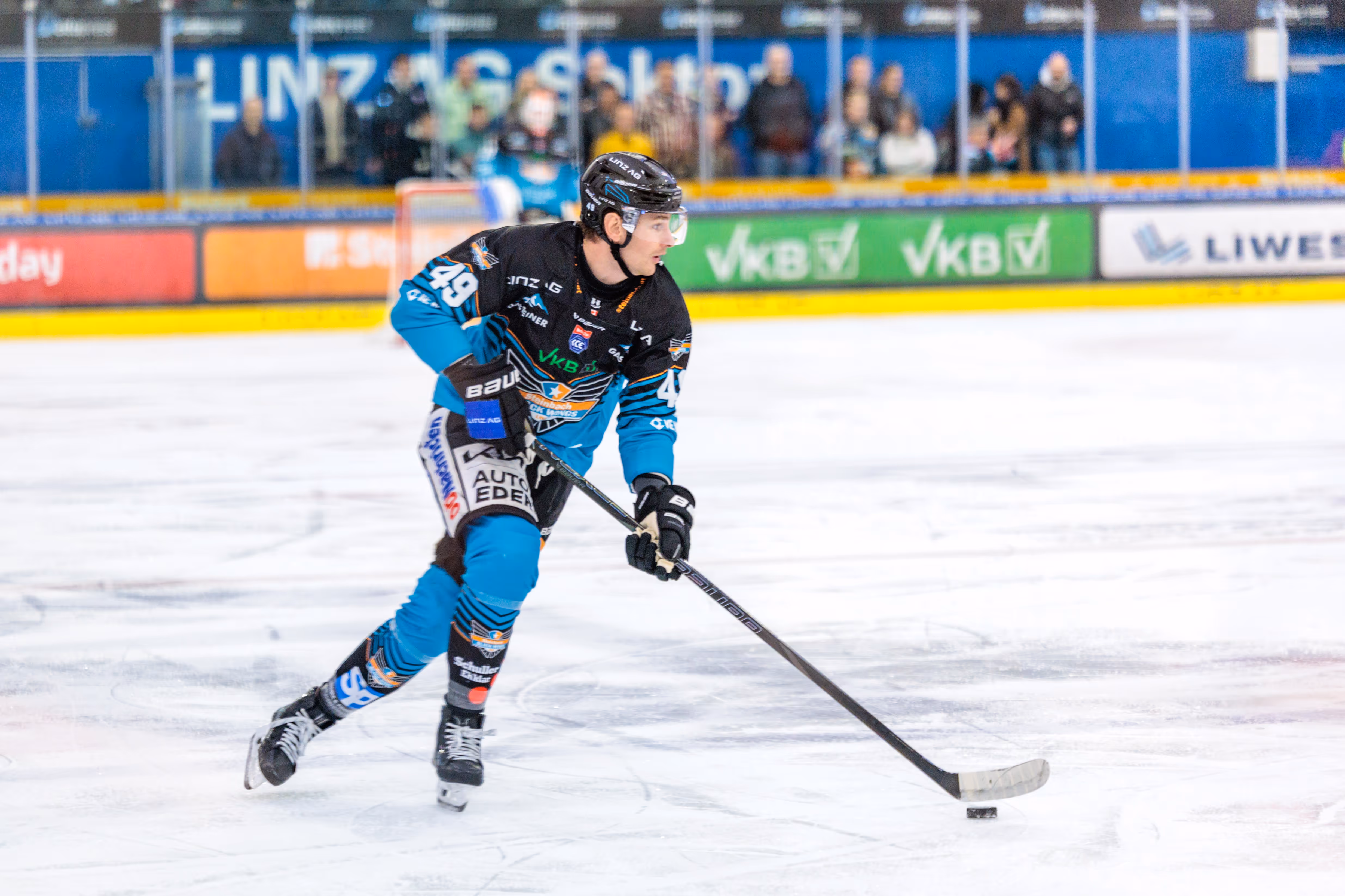 Der Eishockeyspieler Graham Knott von den Black Wings Linz mit der Nummer 49 führt den Puck in voller Aktion während eines Spiels über das Eis