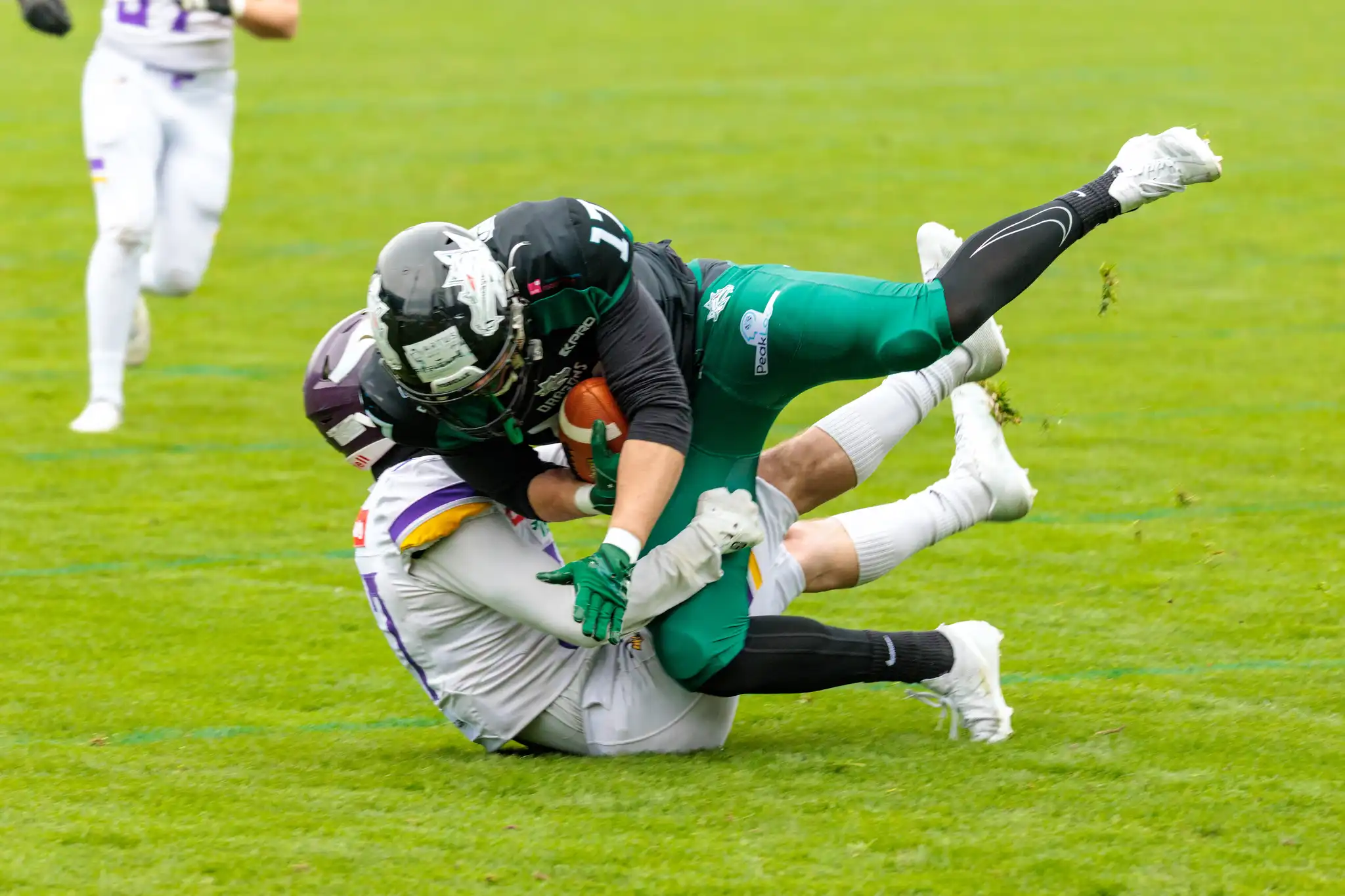 Ein American-Football-Spieler der Danube Dragons im grünen Trikot mit dem Ball wird von einem Vienna Vikings Spieler im weißen Trikot in einem harten Tackle in der Luft gestoppt
