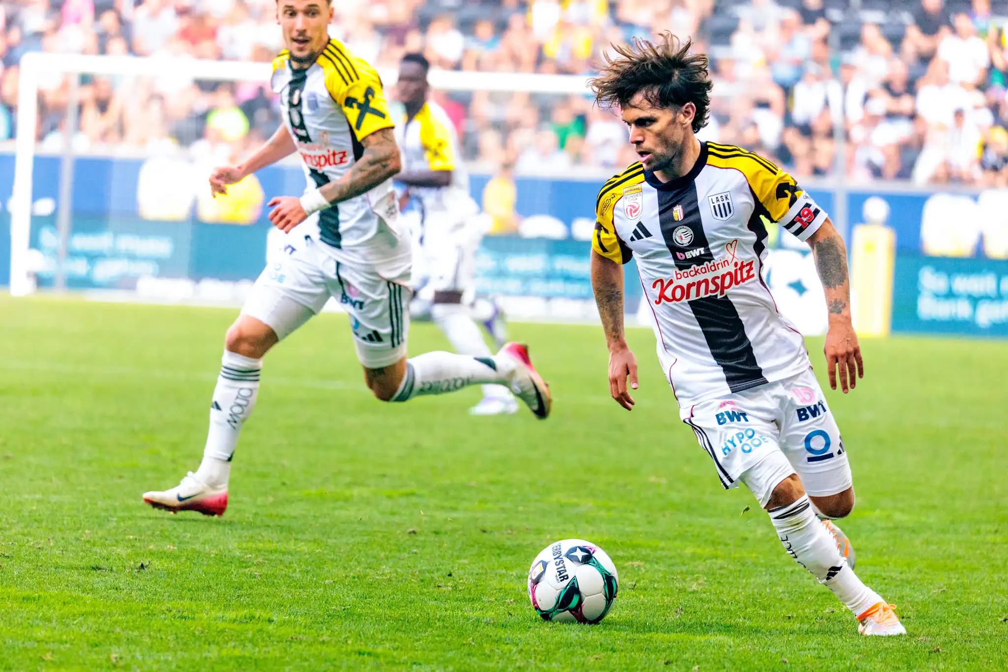 Der LASK-Kapitän Sascha Horvath treibt mit wilder Frisur und konzentriertem Blick den Ball nach vorne
