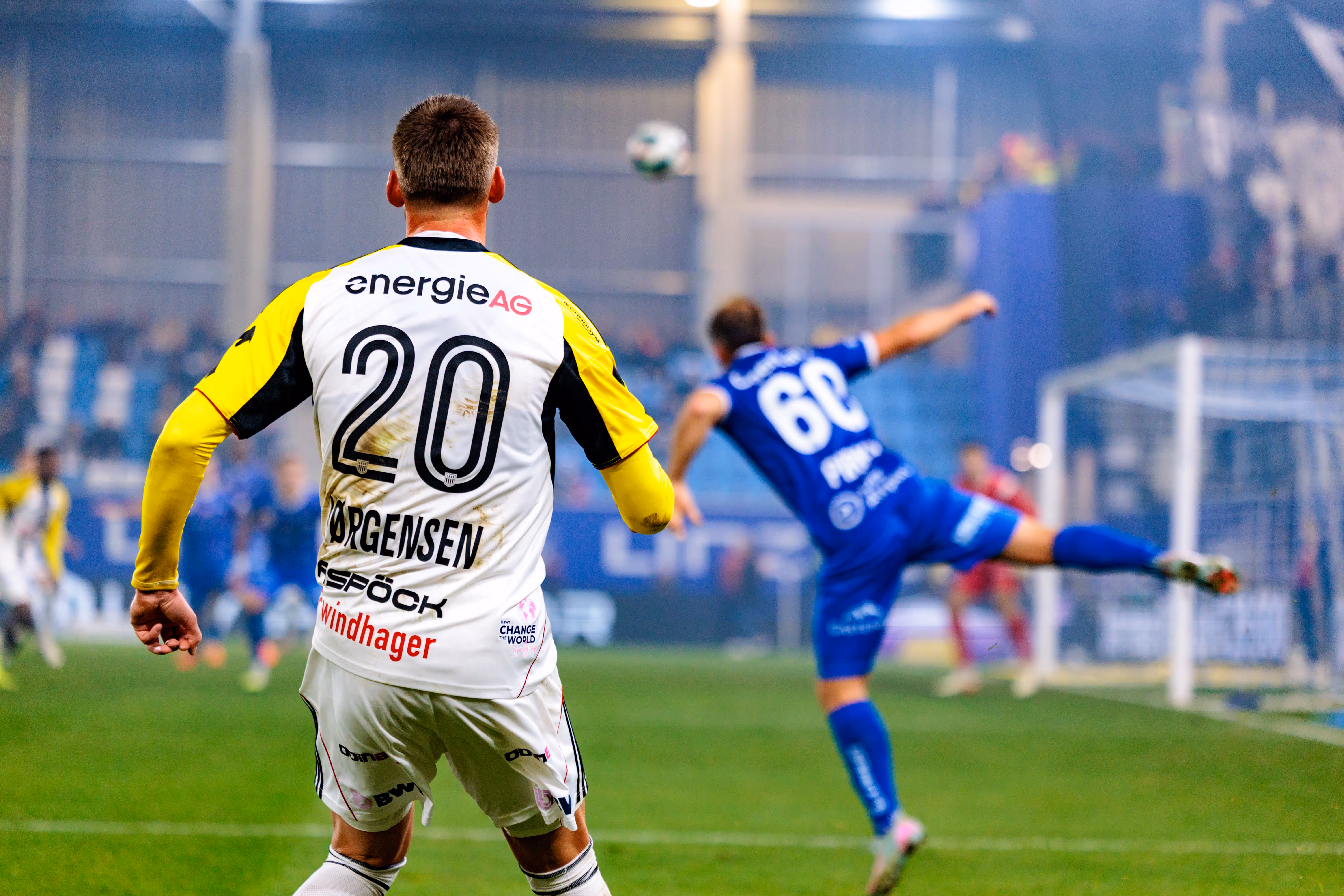 LASK-Spieler Elias Jørgensen mit der Rückennummer 20 beobachtet im Linzer Derby eine Spielszene, während ein Spieler von Blau-Weiß Linz den Ball klärt