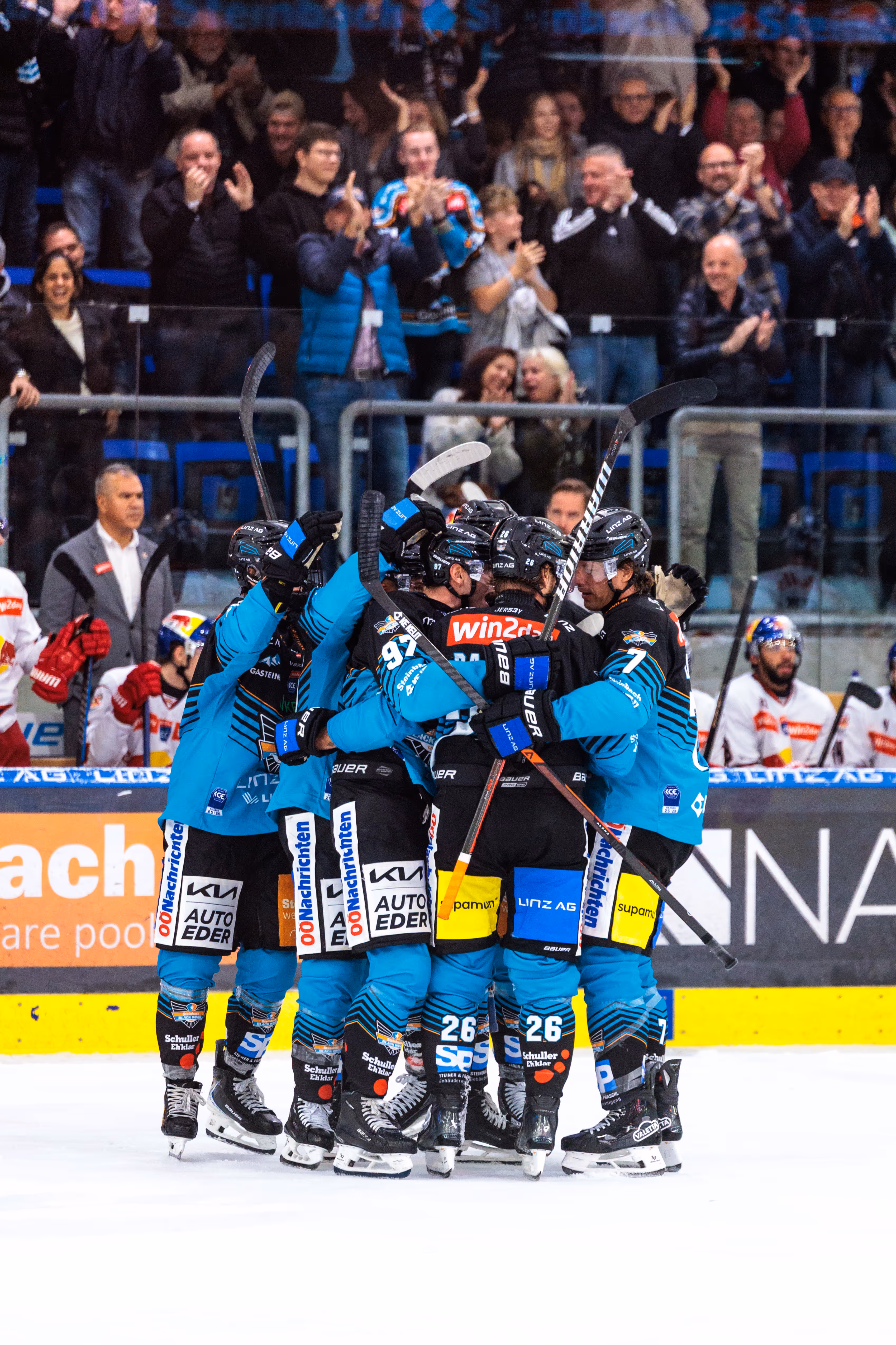 Die Eishockeyspieler der Steinbach Black Wings Linz feiern ihren Sieg mit einer emotionalen Jubeltraube auf dem Eis vor den applaudierenden Fans