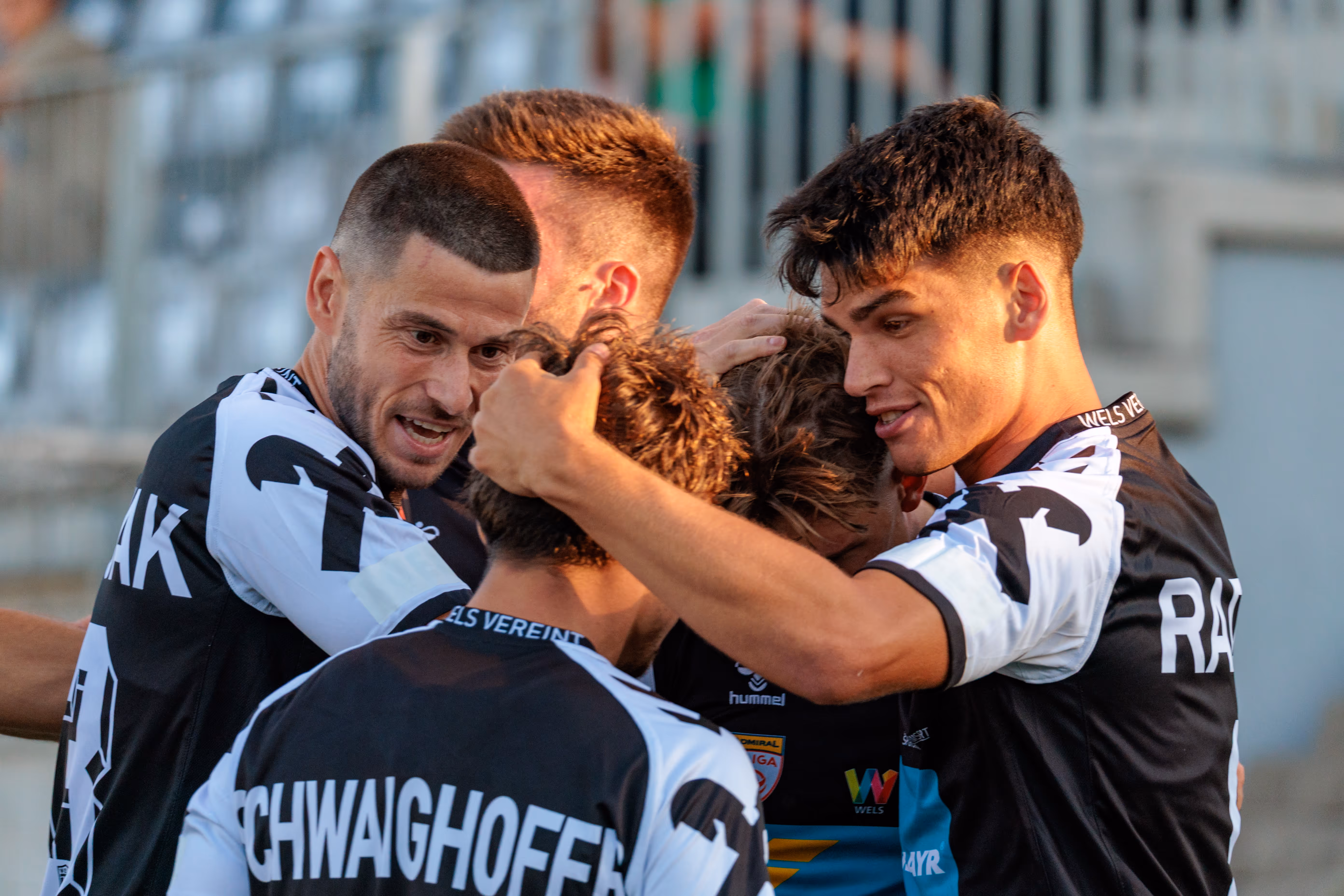 Eng umschlungene Fußballspieler des SPG HOGO Wels teilen freudig ihren emotionalen Torjubel in einem entscheidenden ÖFB-Cup-Spiel