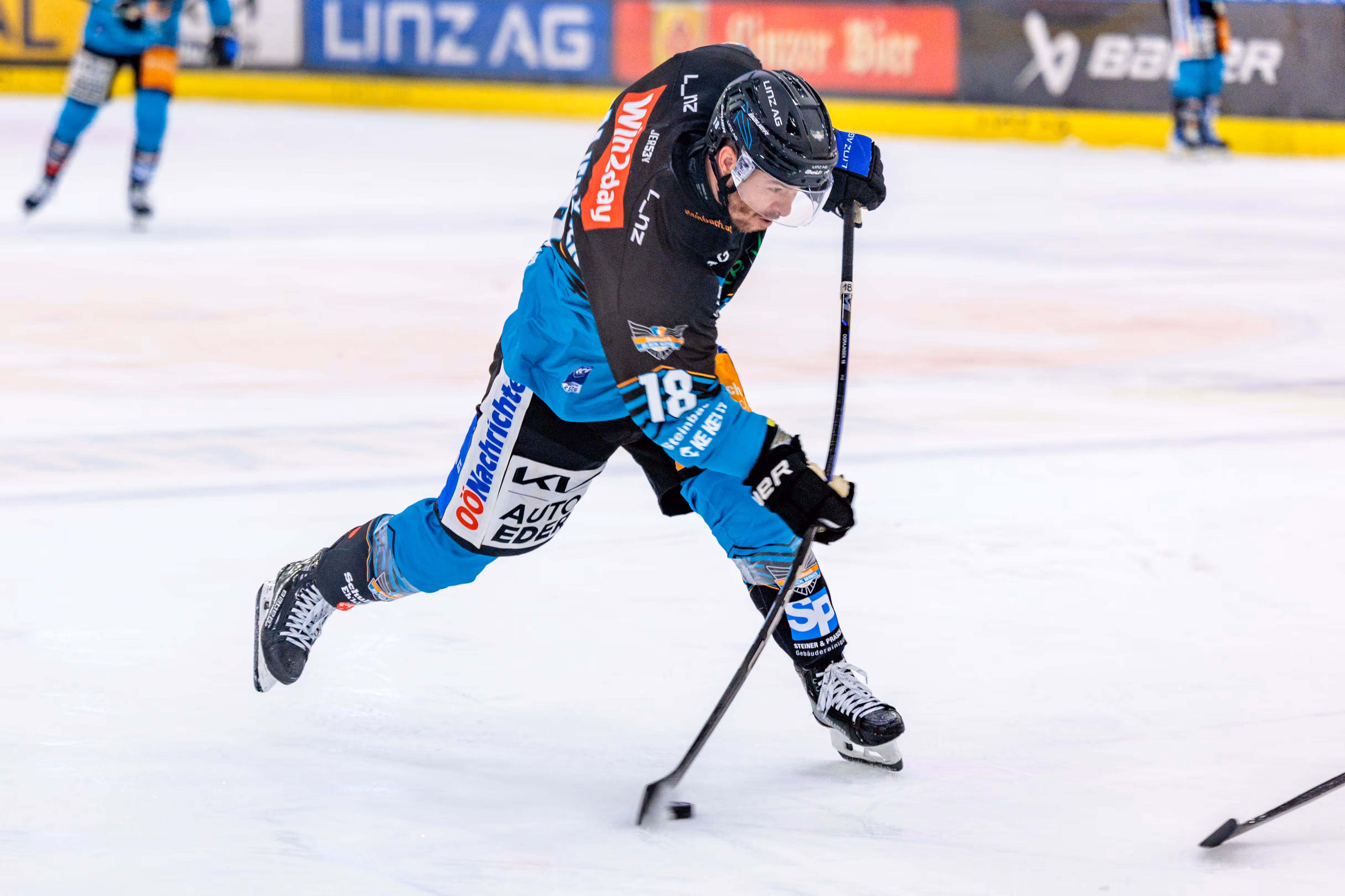 Der Eishockeyspieler Ken Ograjensek von den Steinbach Black Wings Linz gibt in voller Bewegung und tief gebückter Haltung einen kraftvollen Schuss ab