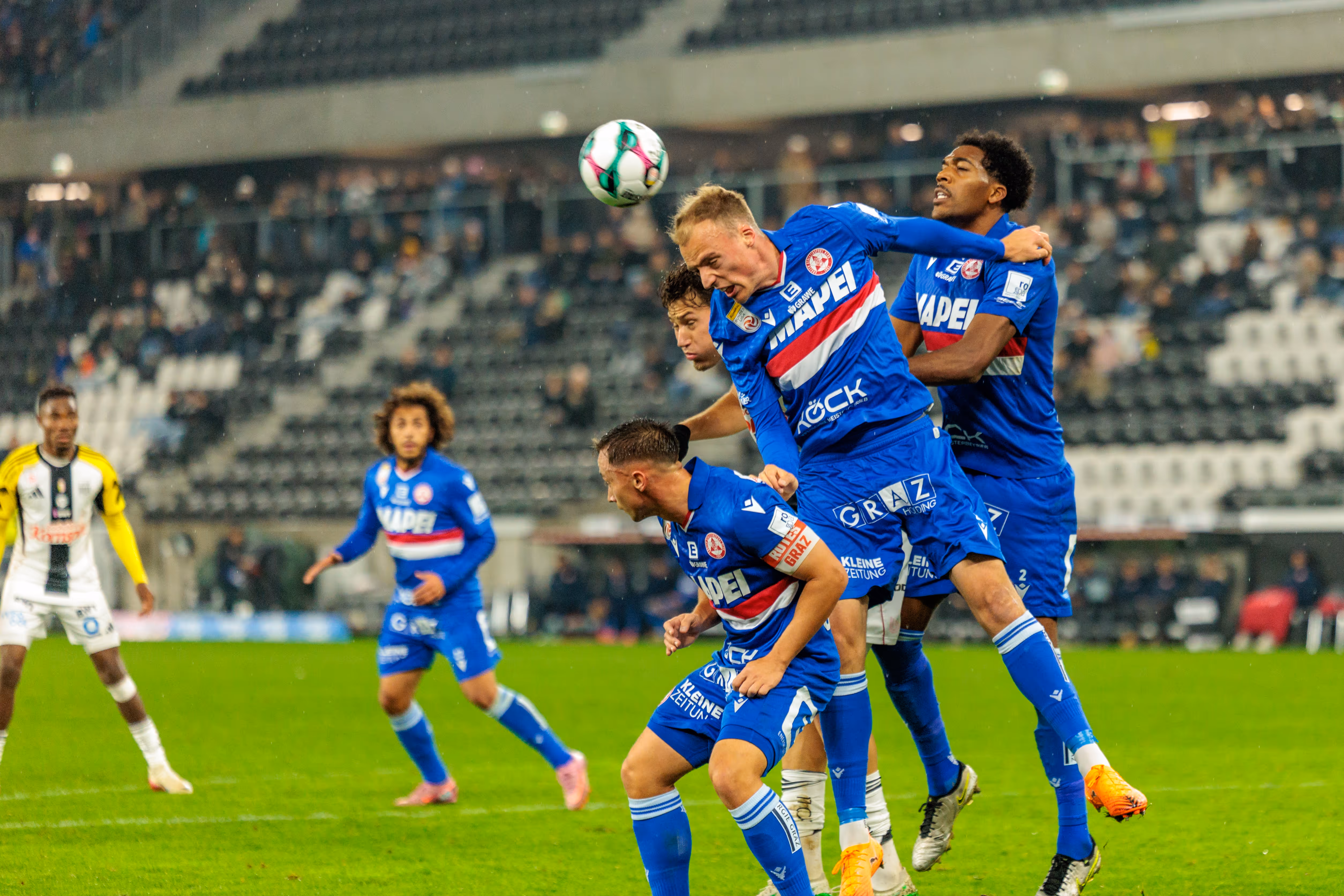 Intensives Kopfballduell eines GAK-Spielers in blauer Dress, der im Spiel gegen den LASK entschlossen zum Ball springt